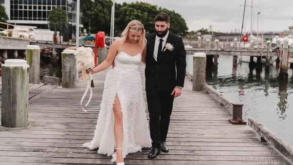 A bride and groom walking together on a wooden dock by the water during their wedding.