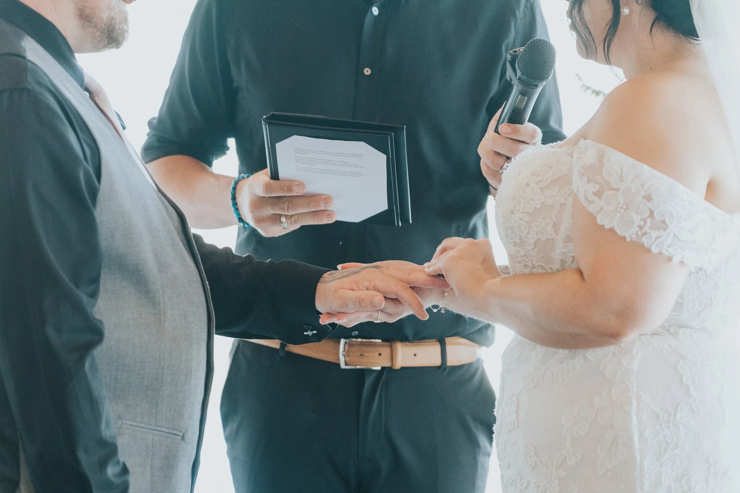 A wedding ceremony with a bride and groom holding hands, exchanging rings, while an officiant officiates.