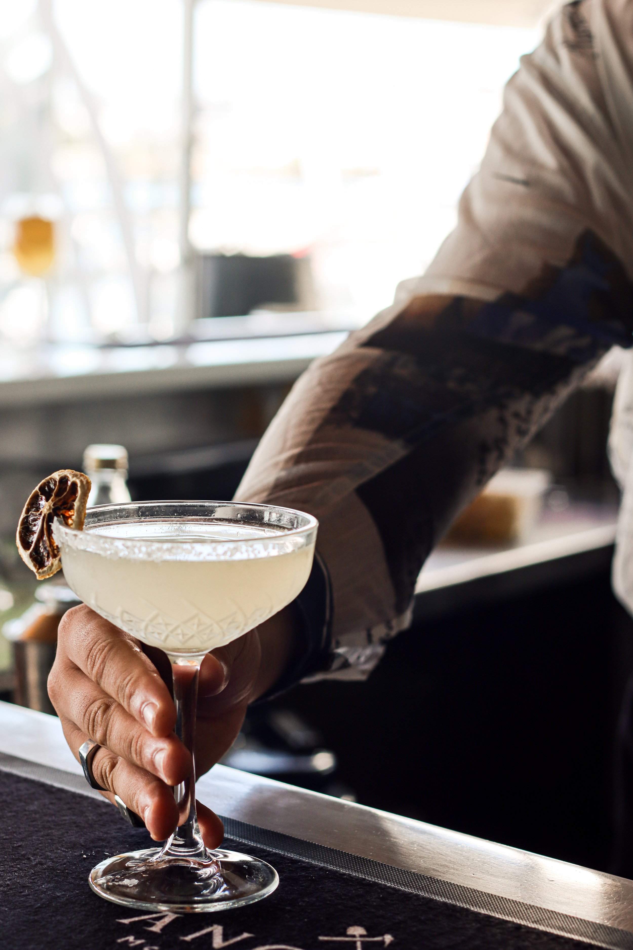 Person holding a cocktail glass with a lemon or lime slice garnish over a bar counter.