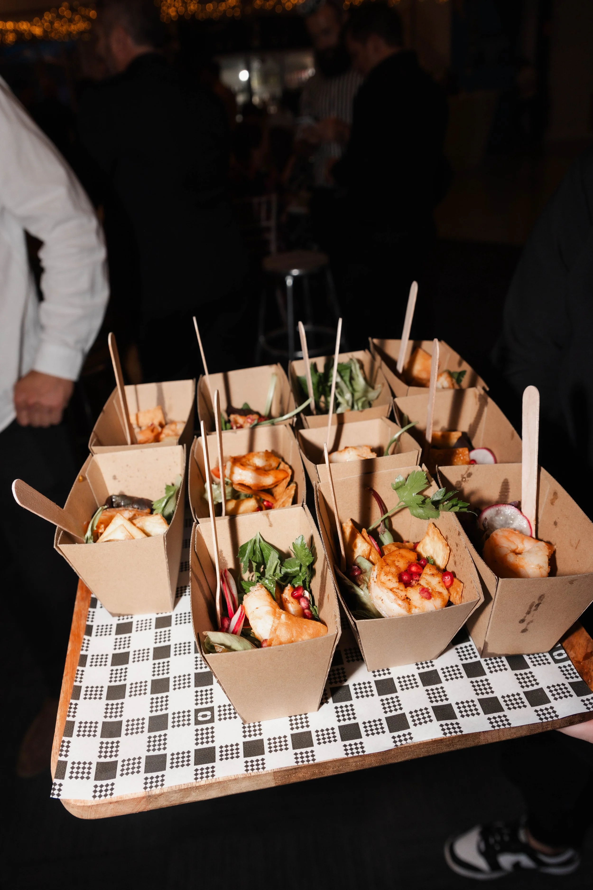 Tray of assorted appetizers in small cardboard containers at a social event.