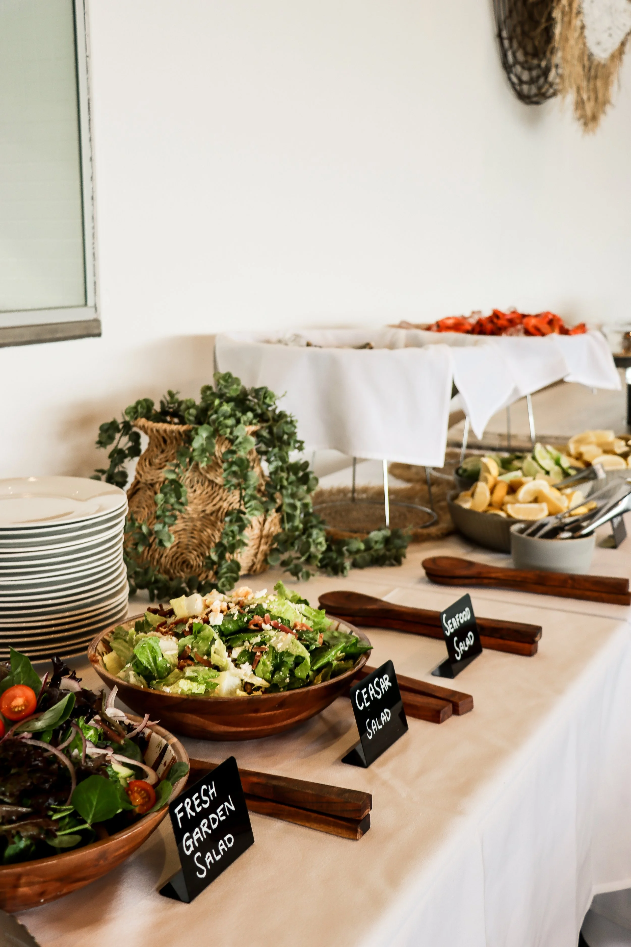 Buffet table with bowls of fresh salads, including garden salad, Caesar salad, and seafood salad, with plates and utensils.