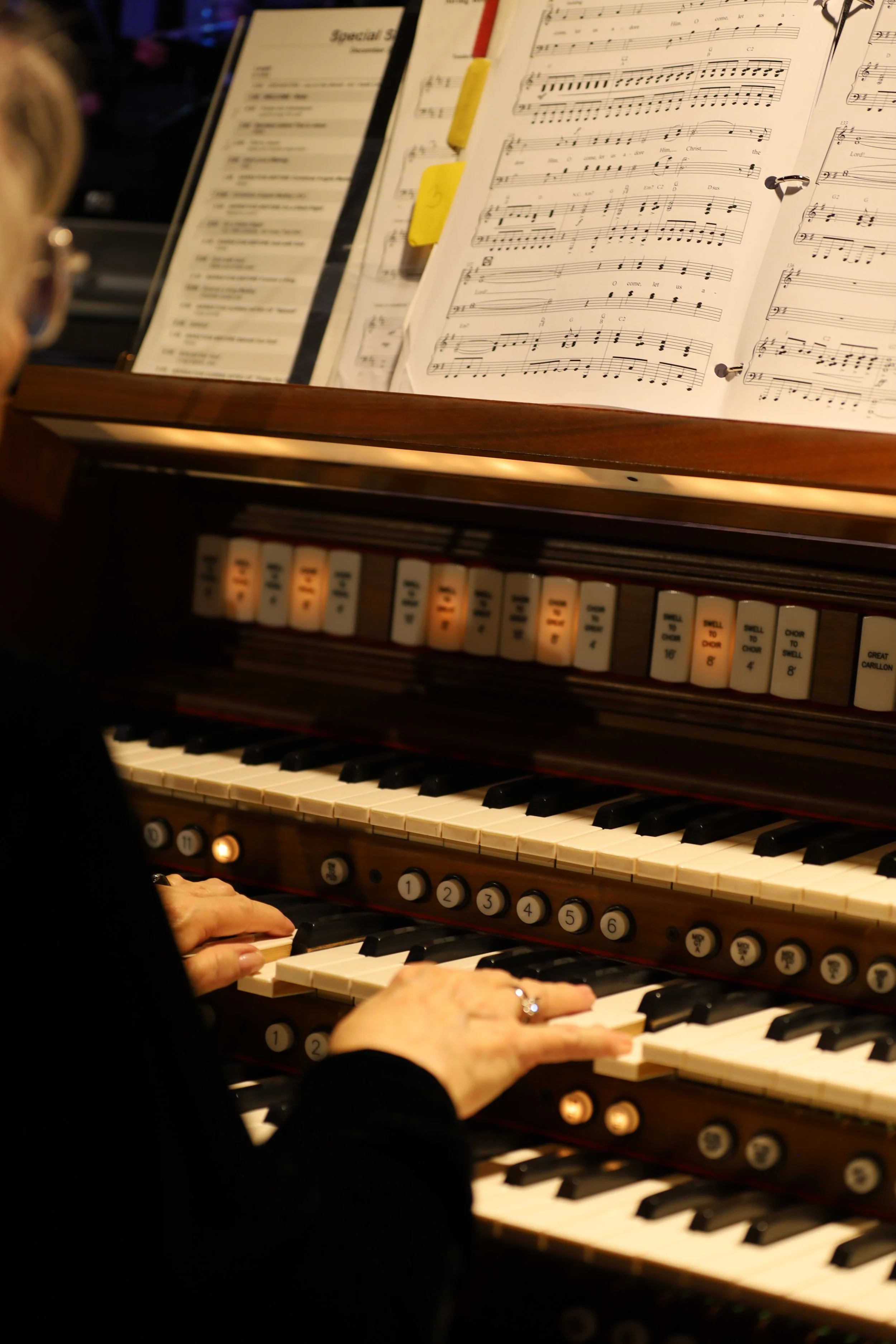 Close-up of a person playing an organ with sheet music and music folders above the keyboard.