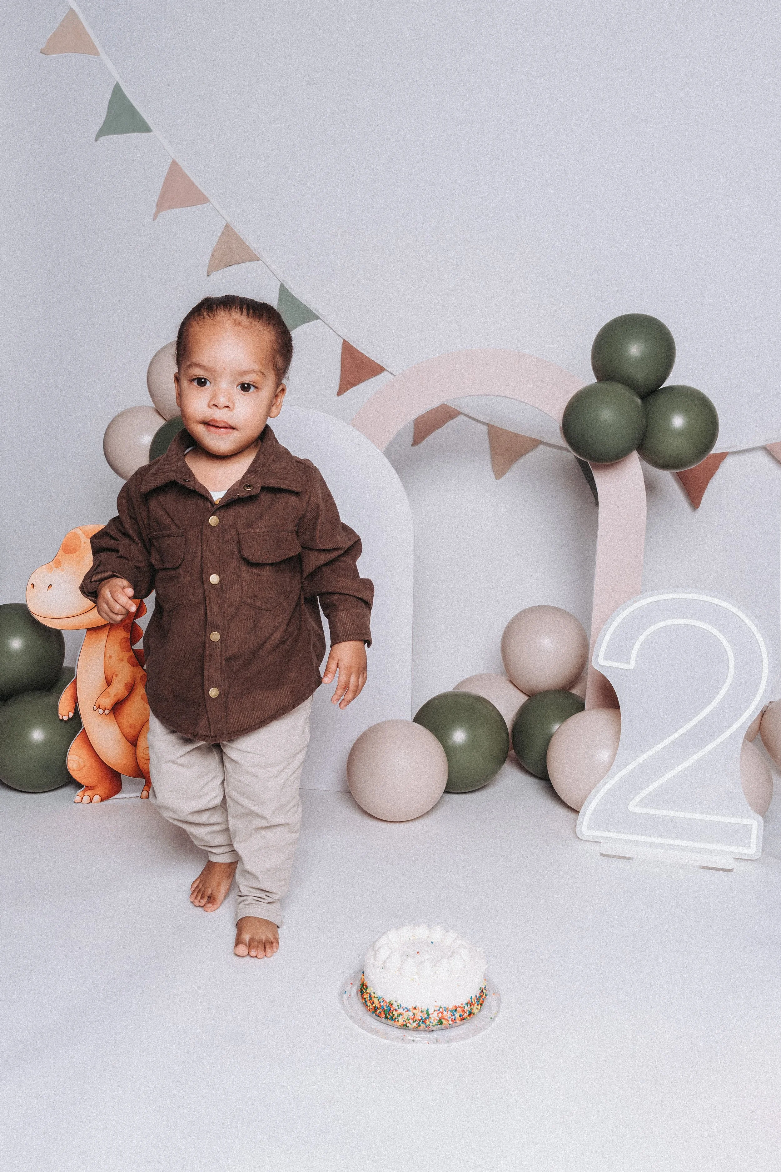 Young boy celebrating his second birthday with a cake, balloons, and birthday decorations.