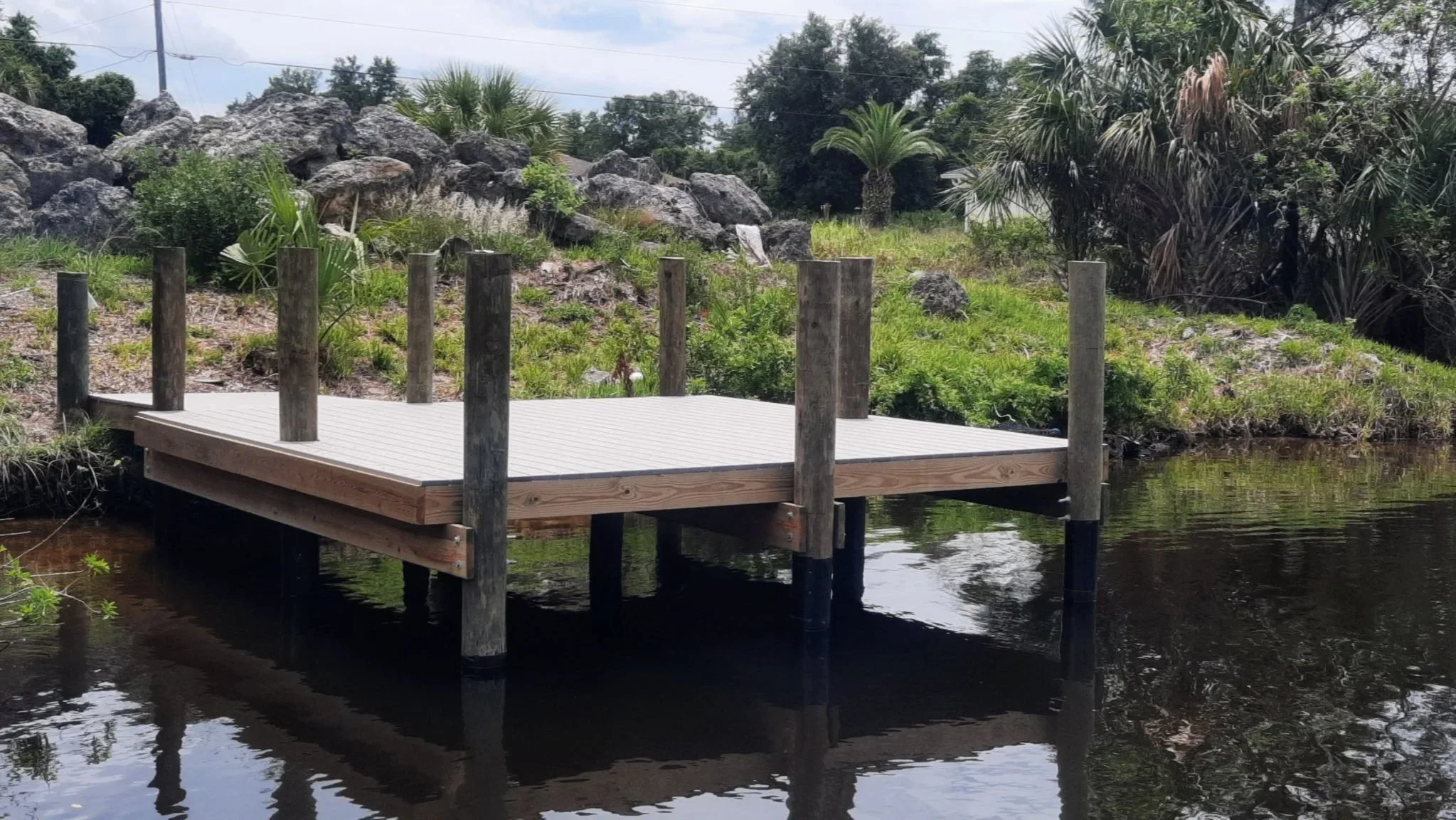 A small wooden dock extends over a calm river with surrounding greenery and rocks in the background.