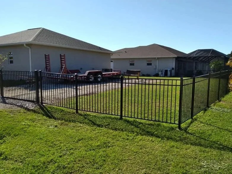 Backyard with a black metal fence, lawn, and two houses, one with a screened porch.