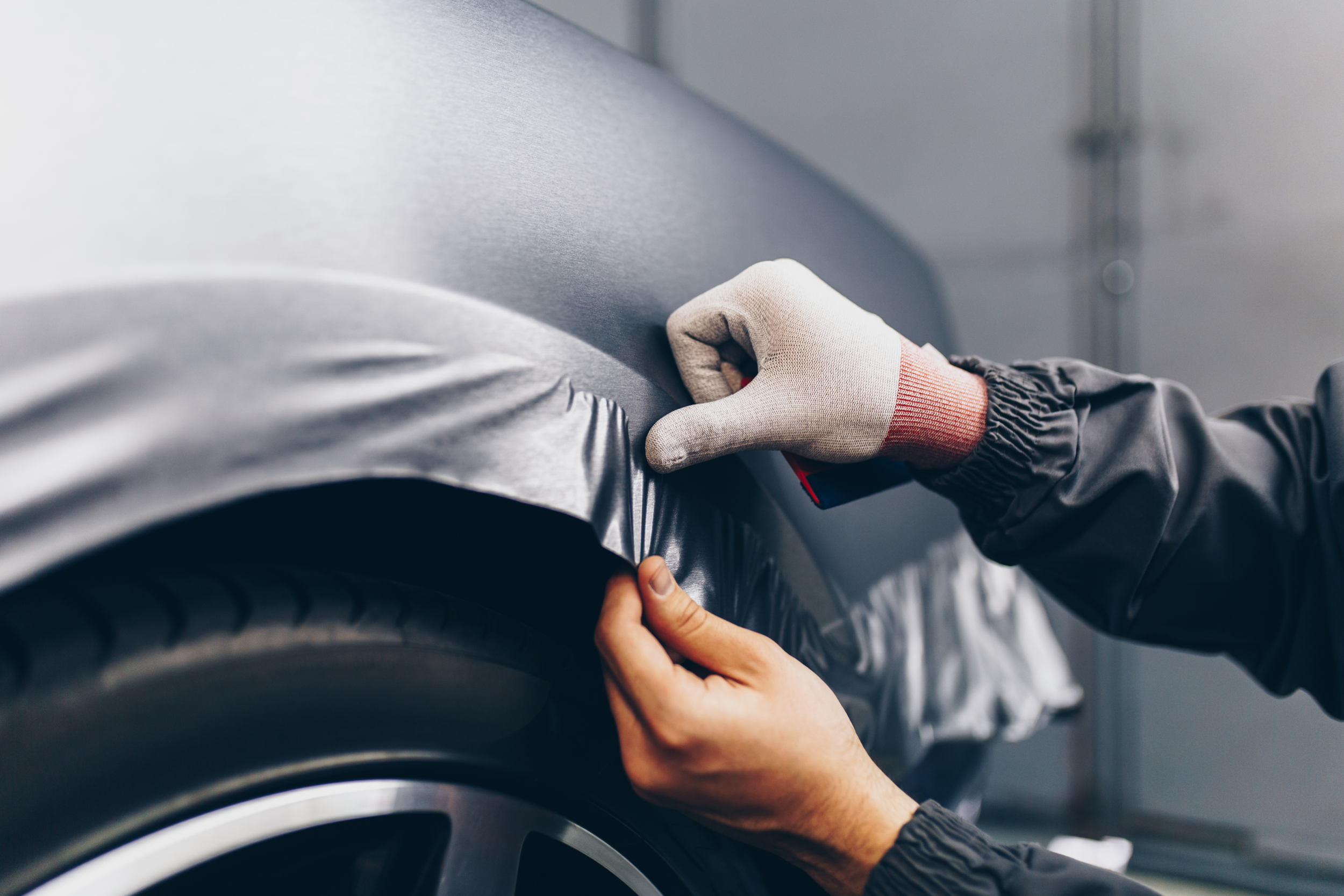 A gloved technician carefully applying paint protection film or vinyl wrap to the body panel of a luxury vehicle, demonstrating the meticulous white-glove installation process at Voiture Noire