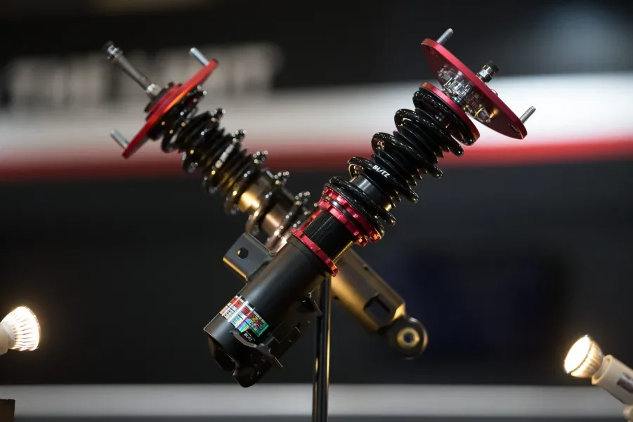 A pair of red and black adjustable performance coilover suspension units crossed against a dark background, showcasing precision-engineered components for sport and luxury vehicle handling upgrades