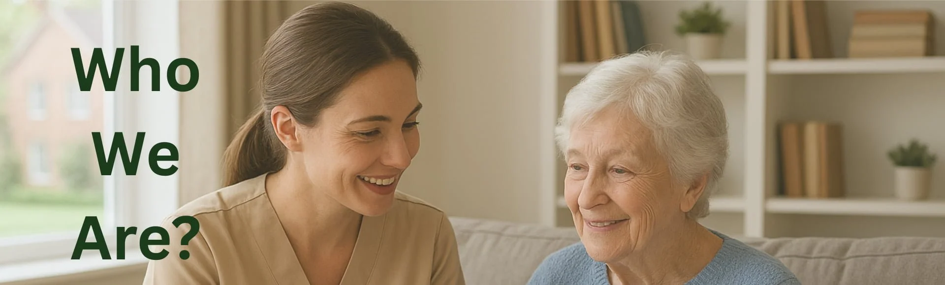 A young woman and an elderly woman sitting together on a sofa, smiling and engaging in conversation in a cozy living room with bookshelves in the background.