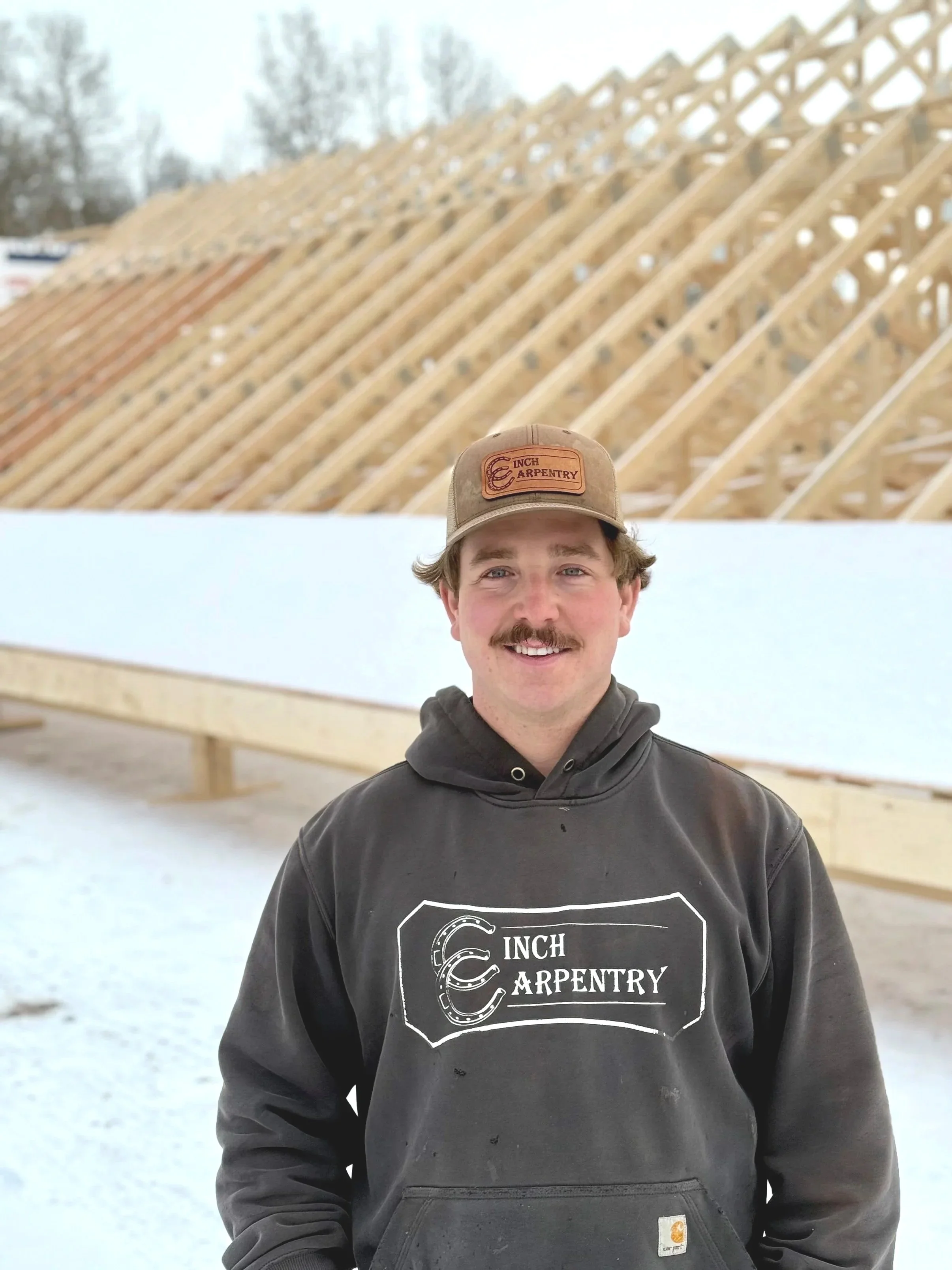 Five men standing together on a stage with a rustic wooden backdrop, holding tools such as hammers and axes, under multicolored string lights. They are smiling and wearing matching hats, suggesting they are celebrating a woodworking or construction event.