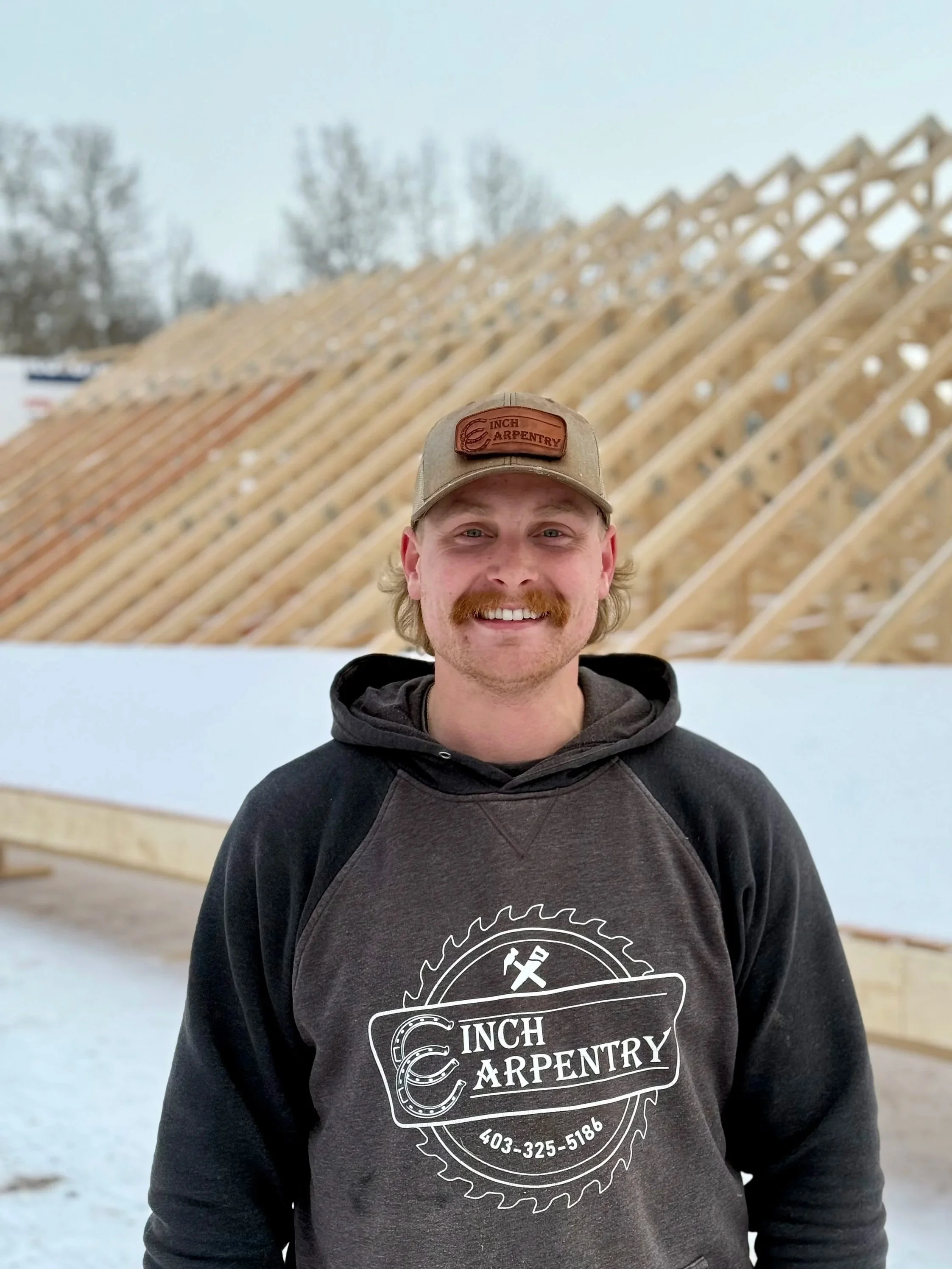 Five men standing together on a stage with a rustic wooden backdrop, holding tools such as hammers and axes, under multicolored string lights. They are smiling and wearing matching hats, suggesting they are celebrating a woodworking or construction event.