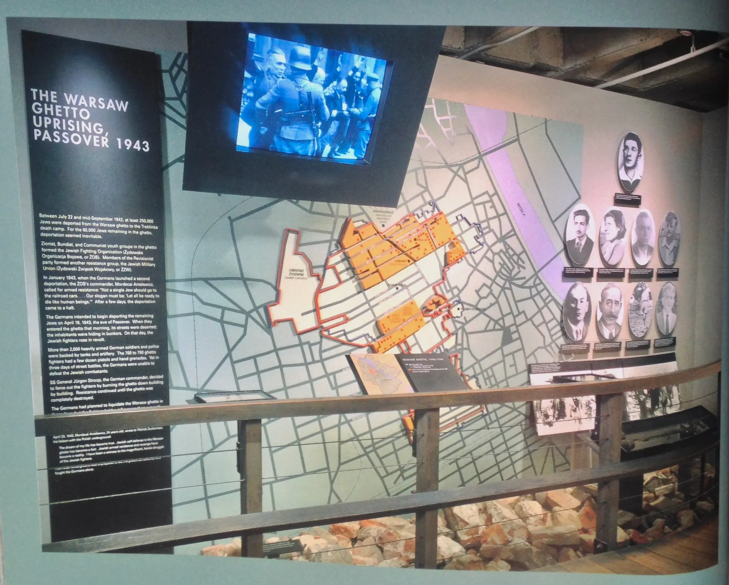 Exhibit about the Warsaw Ghetto Uprising of 1943, featuring a map, photographs of historical figures, and informational text panels.