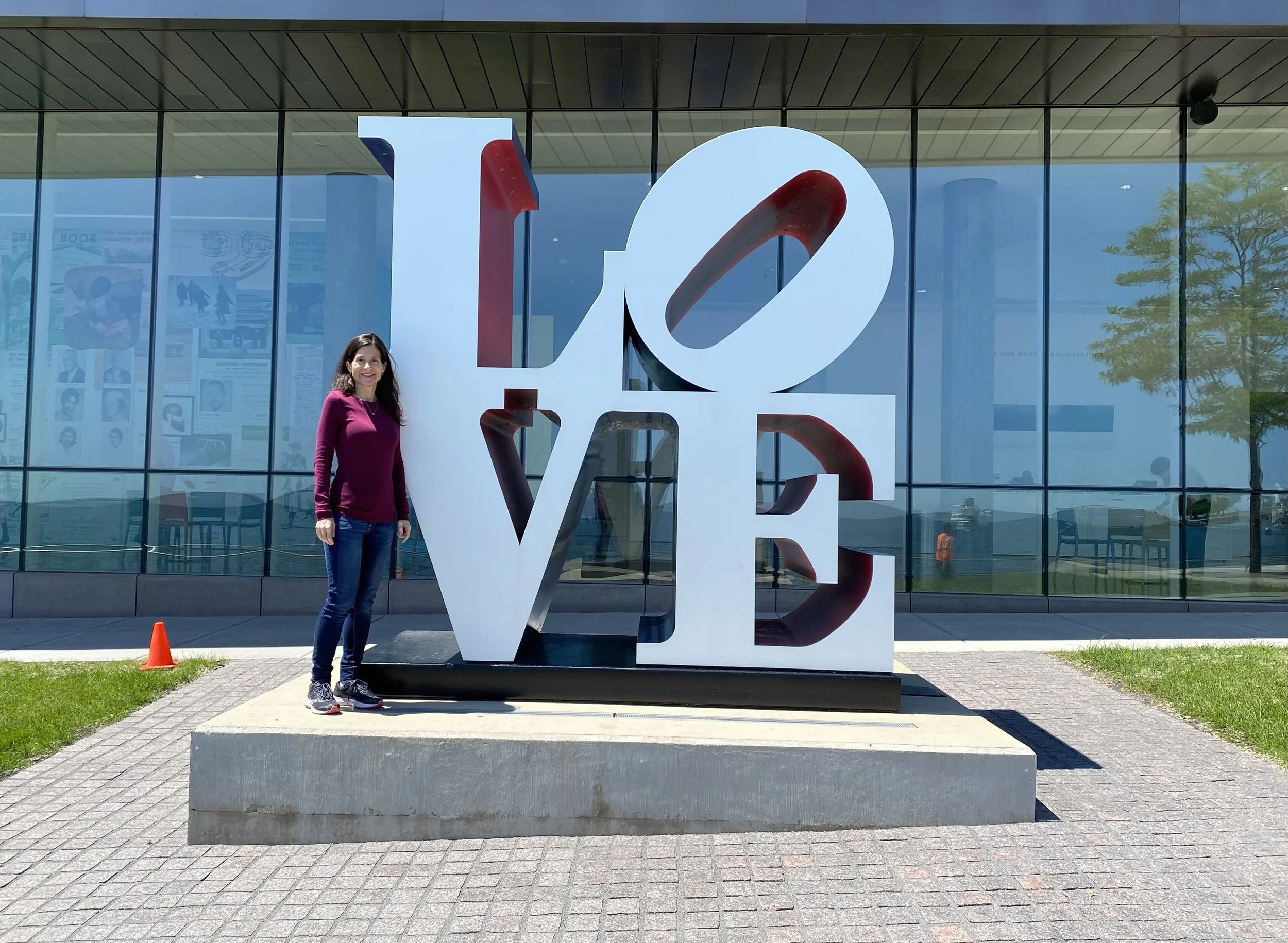 Samantha Baskind standing next to a large sculpture spelling out the word 'LOVE' in front of a glass building.
