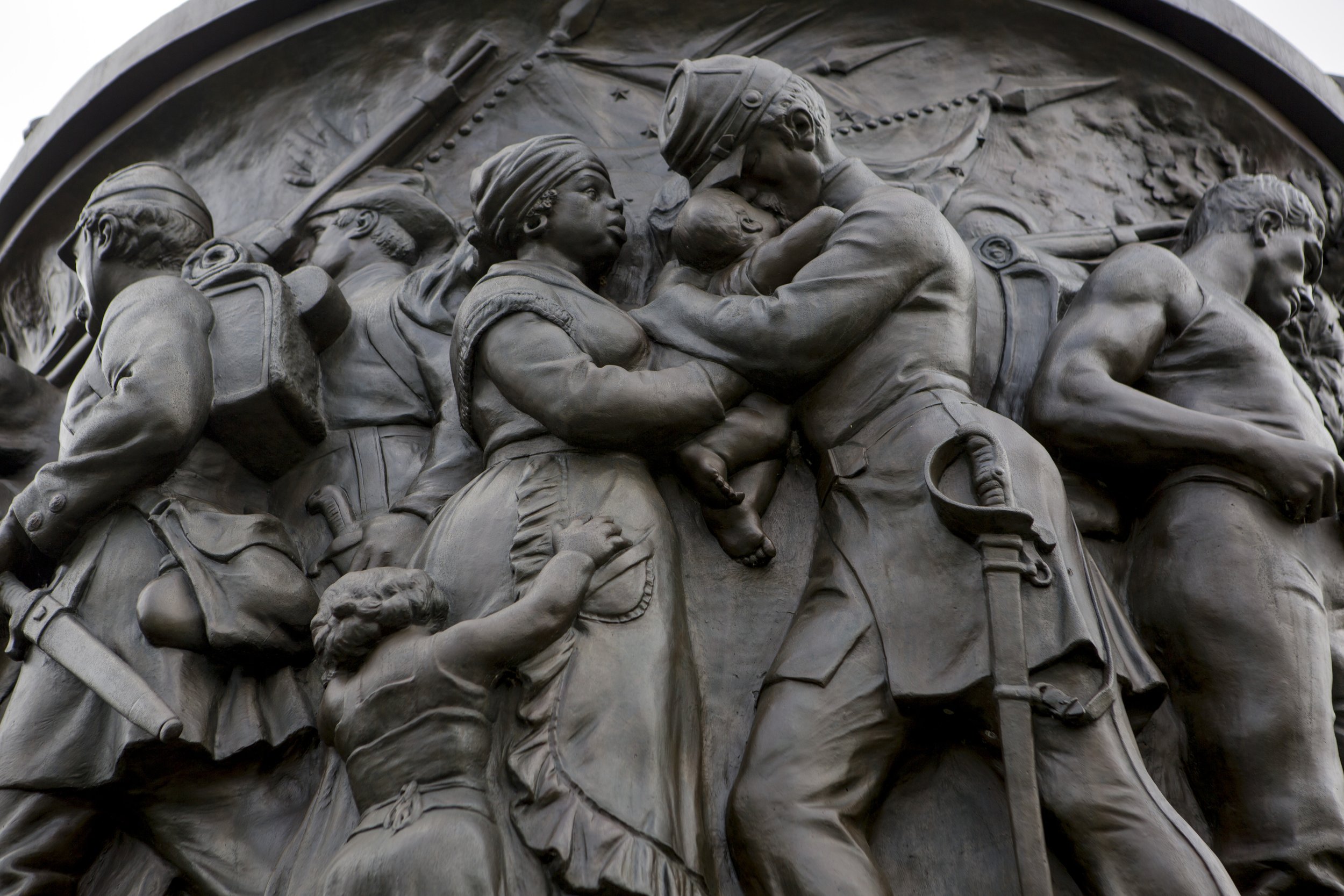 Close-up of a detailed bronze relief sculpture depicting soldiers and civilians from the Civil War era, with a prominent soldier holding a child and a woman, and a young girl reaching up to him.