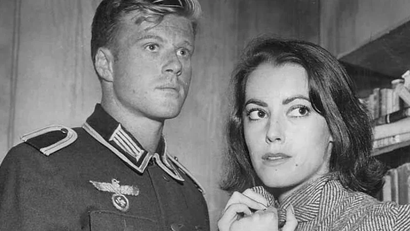 A black and white photograph of a man in a military uniform and a woman standing close together, with the woman holding her collar and looking to the side.