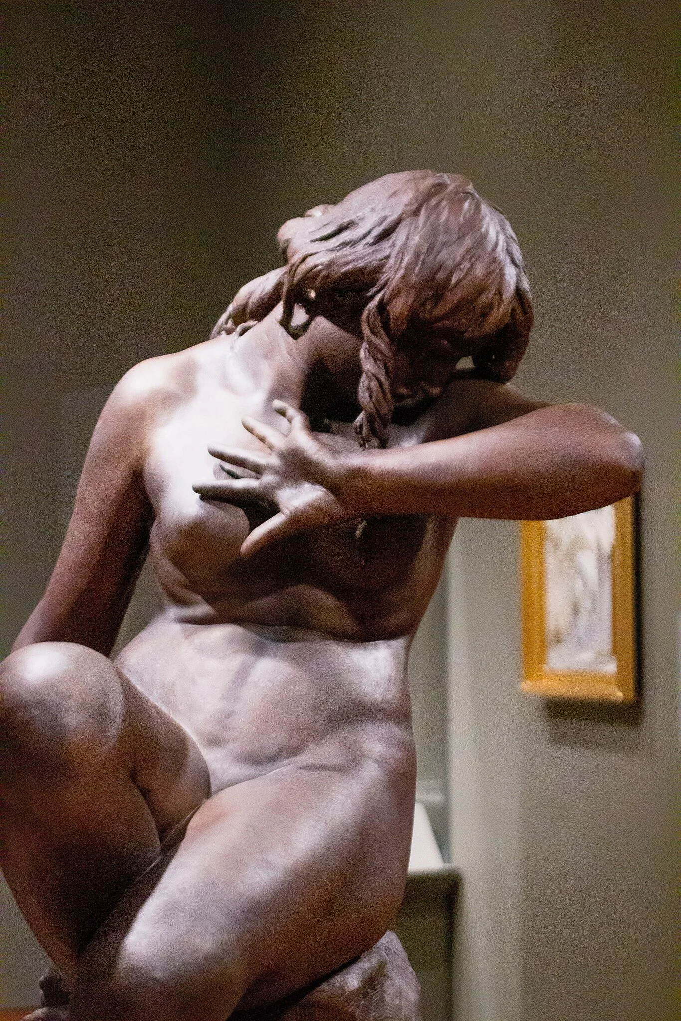 Close-up of a sculpture of a seated woman with her eyes closed and hands crossed over her chest, in an art museum.