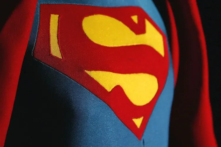 Close-up of Superman logo on costume, featuring a red and yellow 'S' emblem on a blue background.