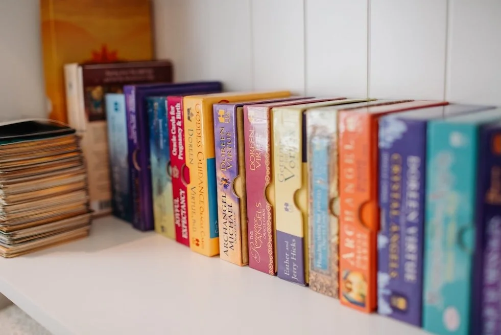 A row of colourful oracle card decks on a white shelf in Tarla's treatment room in Eudlo, Sunshine Coast.