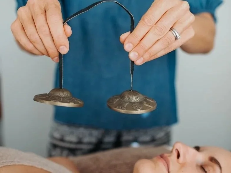 Tarla is holding an instrument over her client lying down.