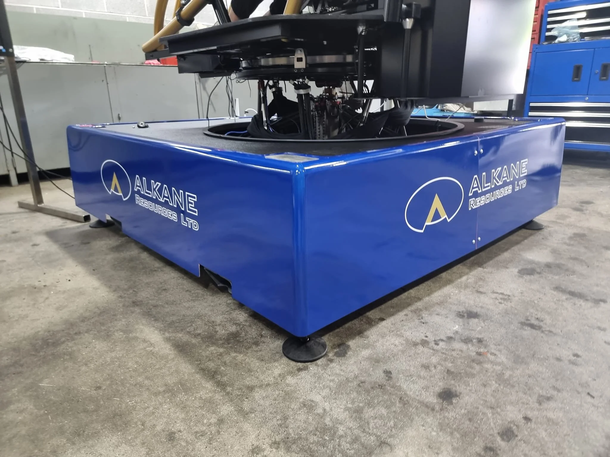 A large blue industrial machine with the logo and name "ALKANE RESOURCES LTD" printed on the side, situated on a concrete floor in a workshop.