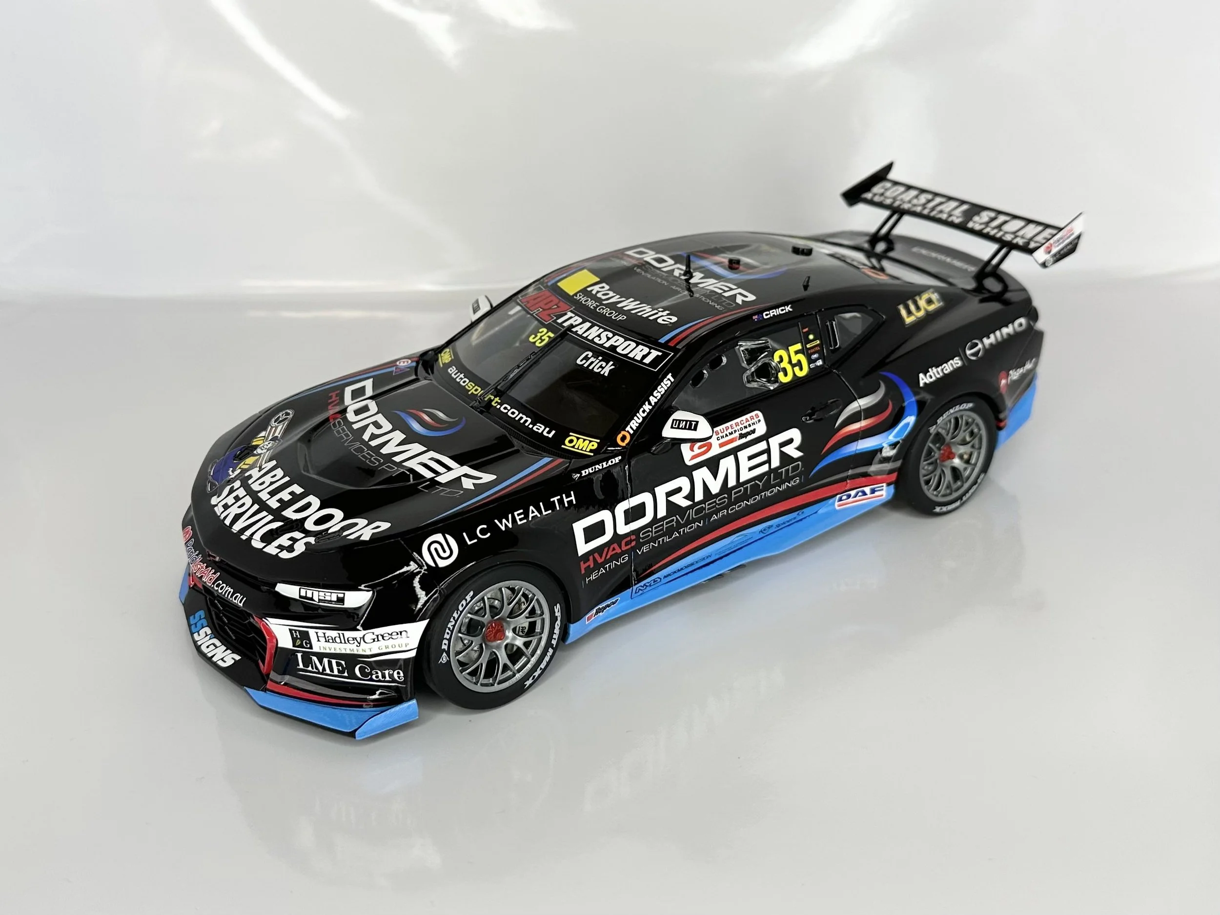 A detailed black remote control car model with racing decals, sponsor logos, a rear wing, and silver wheels, placed on a white surface.