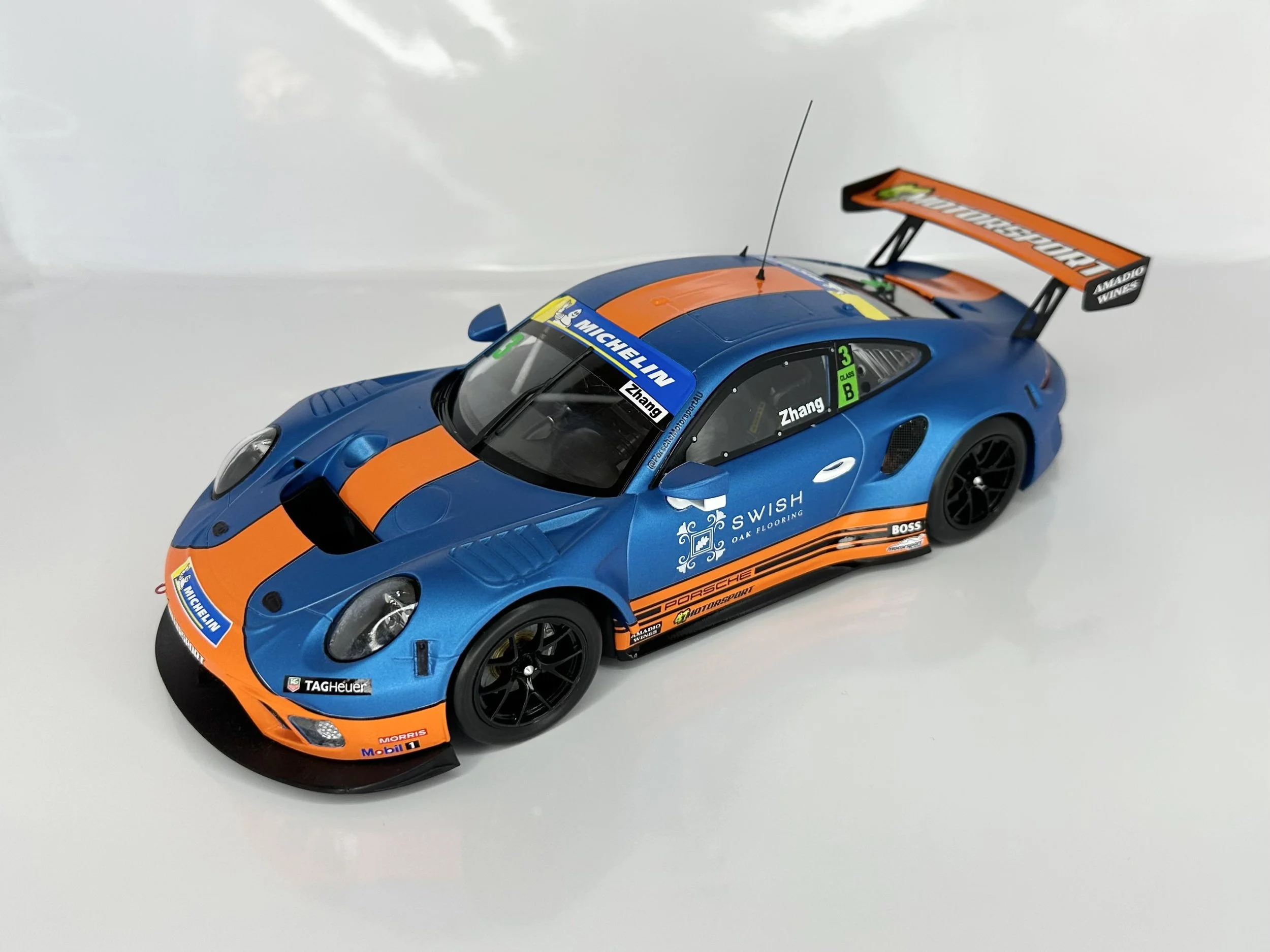 A detailed model race car in blue and orange with various sponsor decals, a large rear wing, and racing number and driver name stickers.