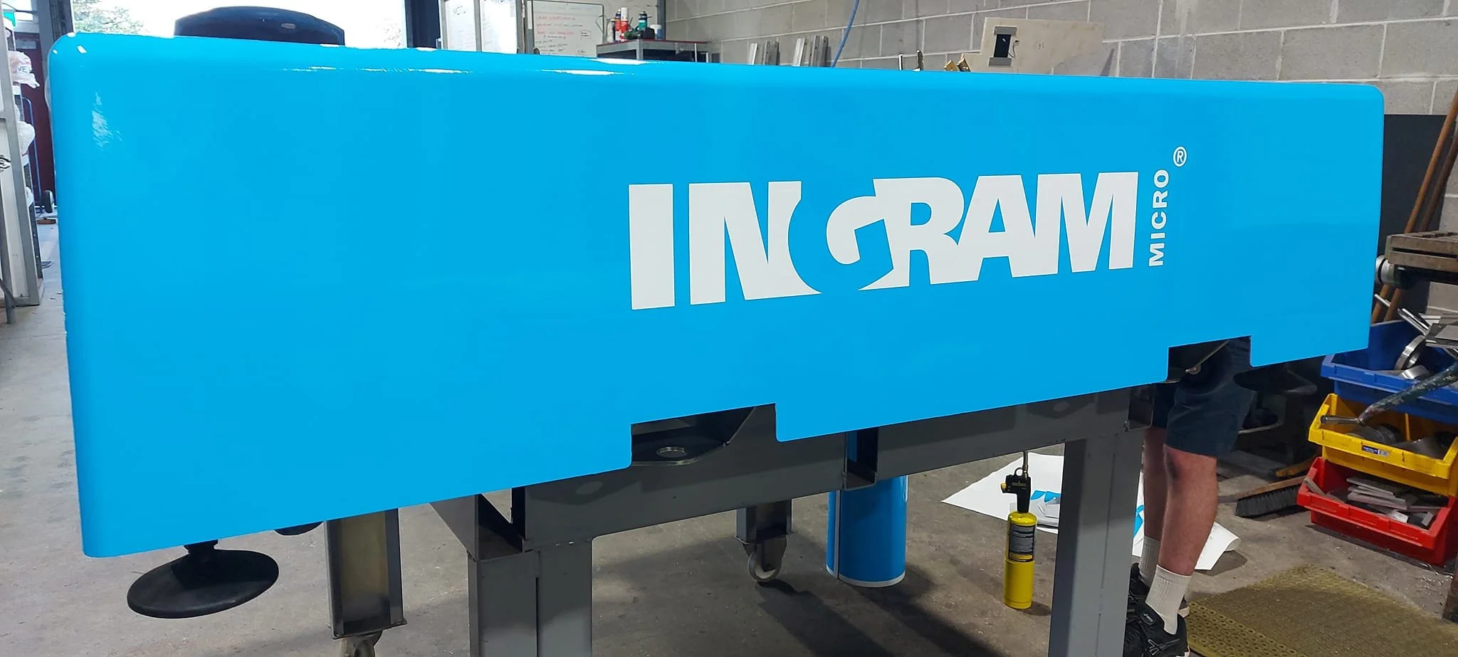 A large blue machine with the words INGRAM MICRO written on it, located in a workshop or warehouse environment.