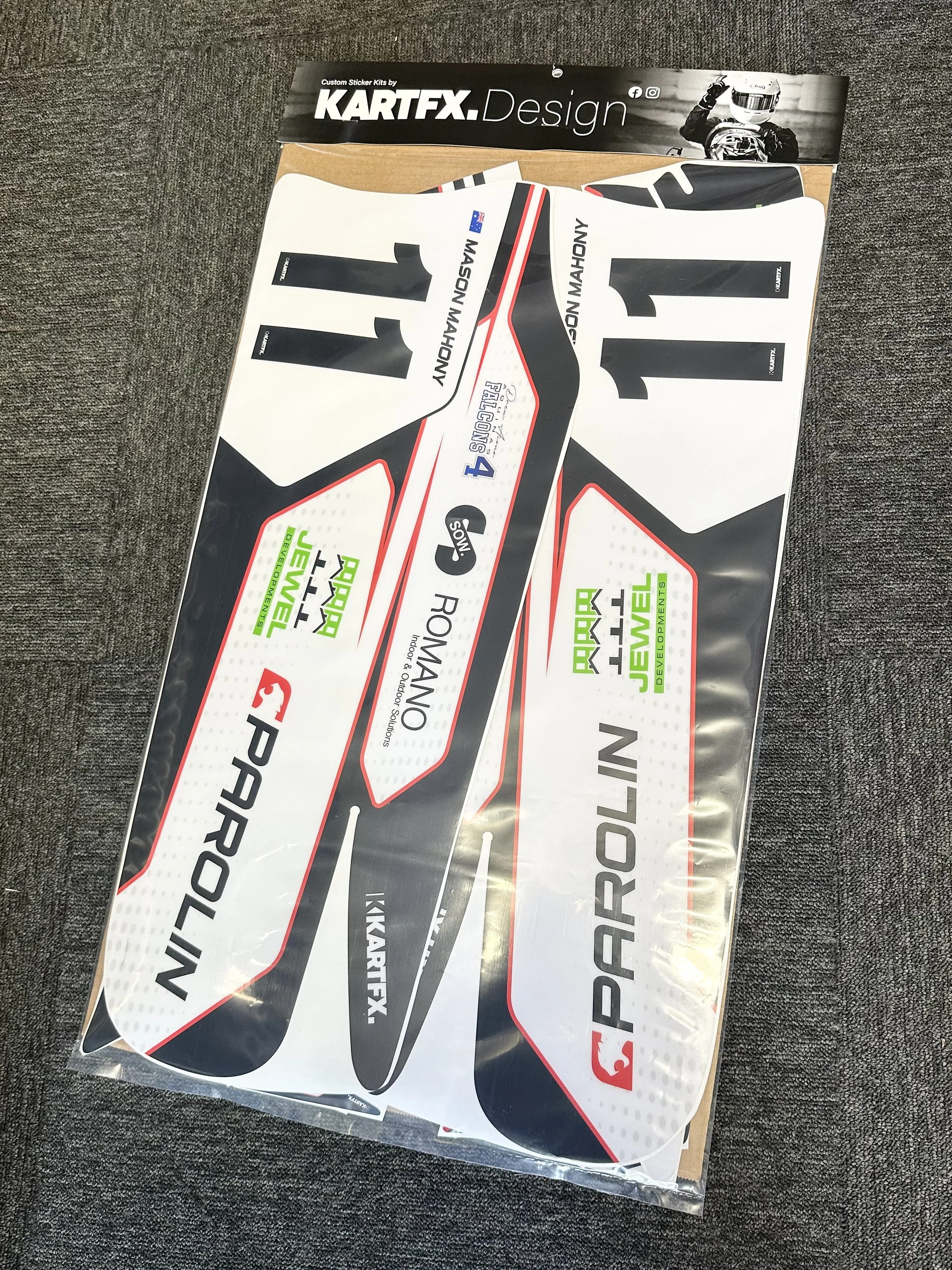 A sheet of car racing decals featuring the names Prolor, Roman Noy, and the number 11, along with various sponsor logos, placed on a fabric surface.