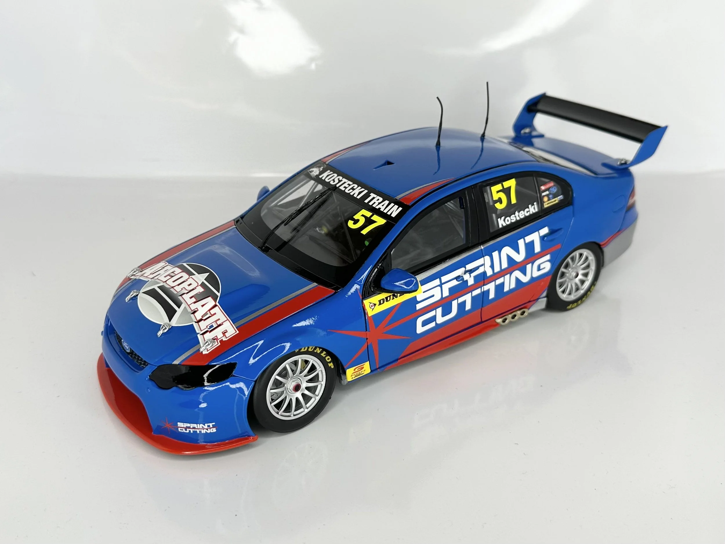 A detailed model of a racing car with a blue, red, and black color scheme, featuring sponsor logos like Sprint Cutting and Delta Force, with the number 57 and license plate KOSTECKI TRAIN.