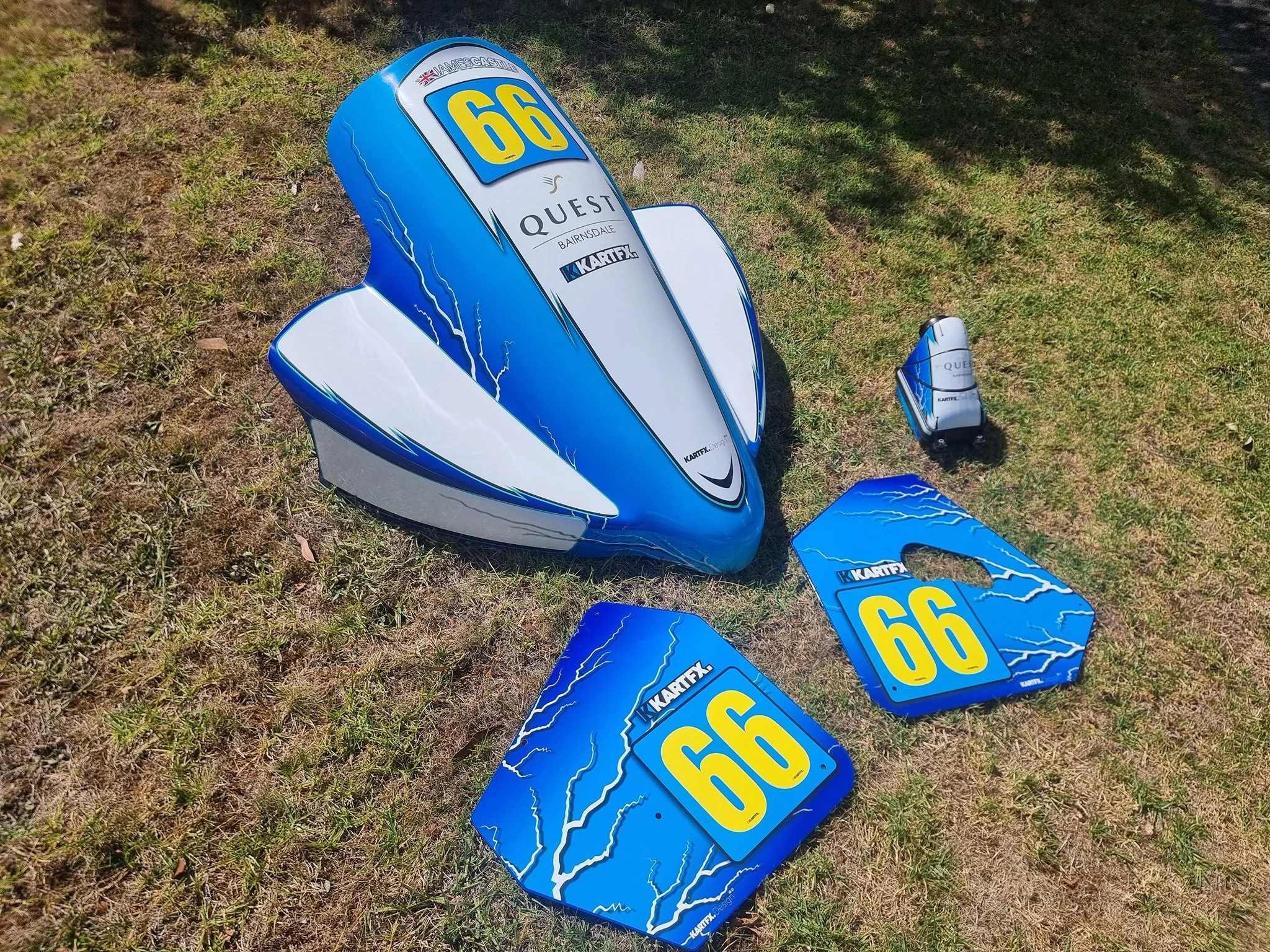 Blue motorcycle fuel tank, side panels, and number plates with yellow numbers 66 and 99, all decorated with lightning bolt graphics, laid on grass ground.