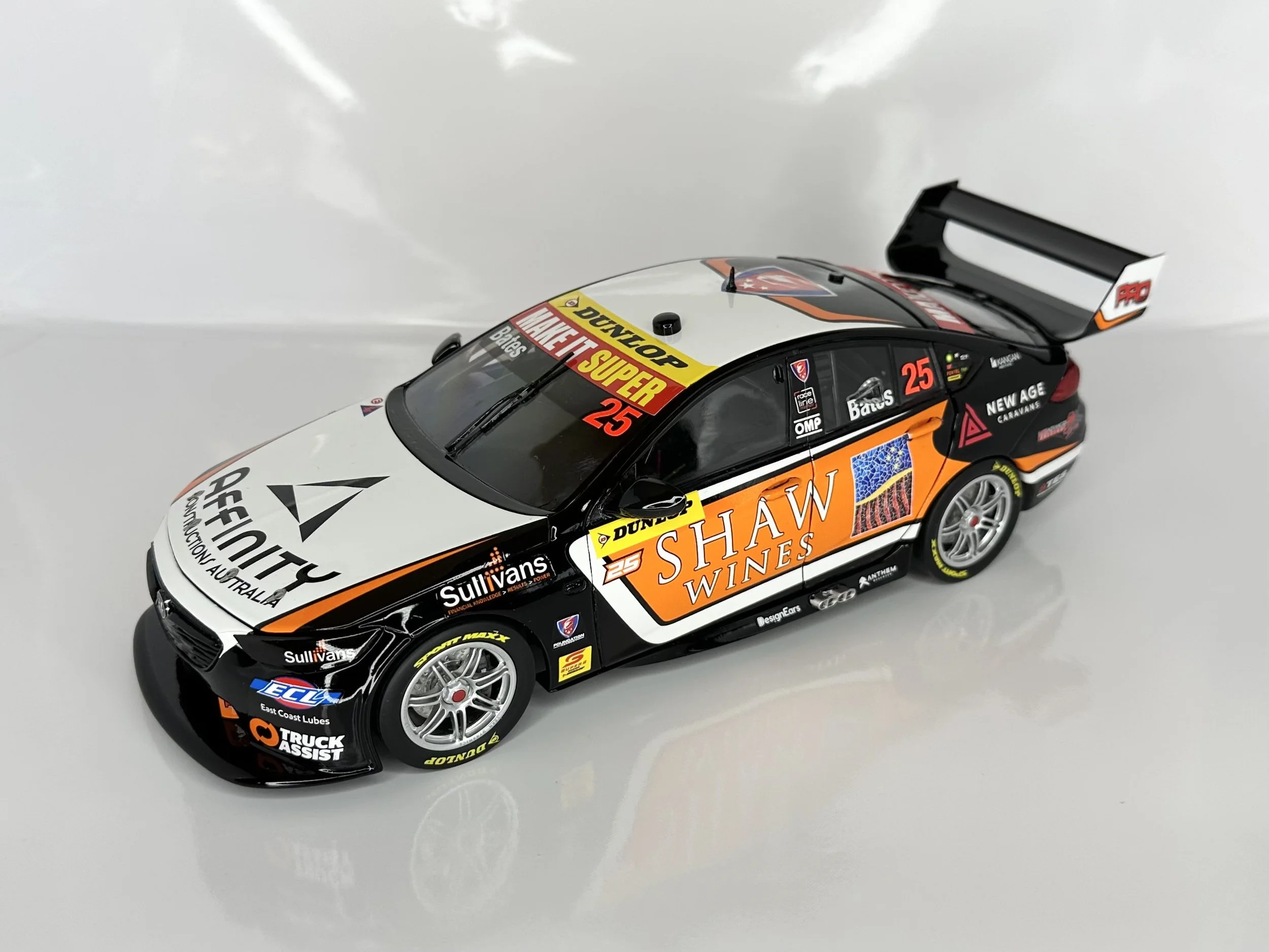 A black, white, and orange scale model race car with various sponsor logos and the number 25, featuring a large rear wing.