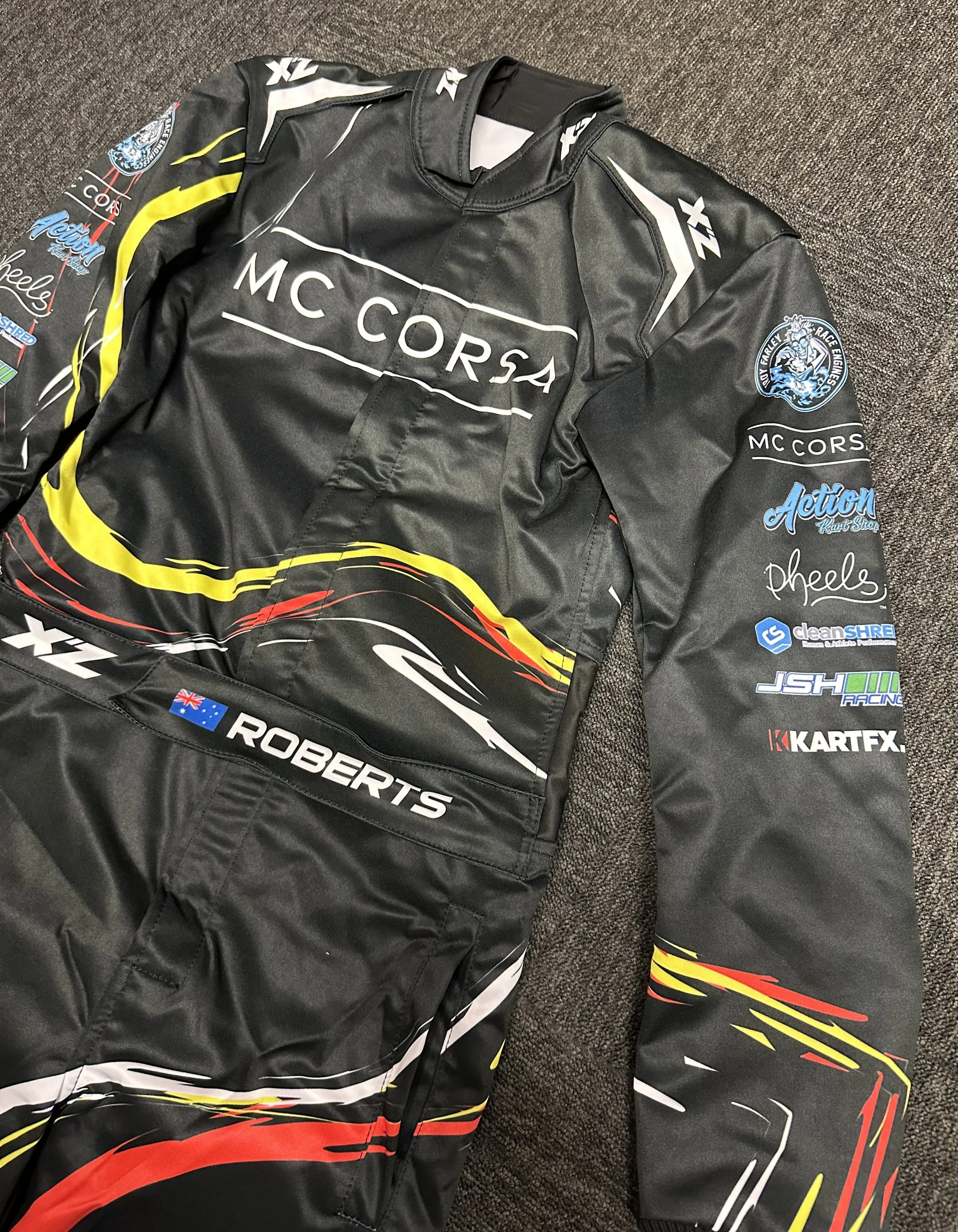 Black racing suit with various sponsor logos, including McCorsa and Roberts, and colorful yellow, red, and white graphic design.
