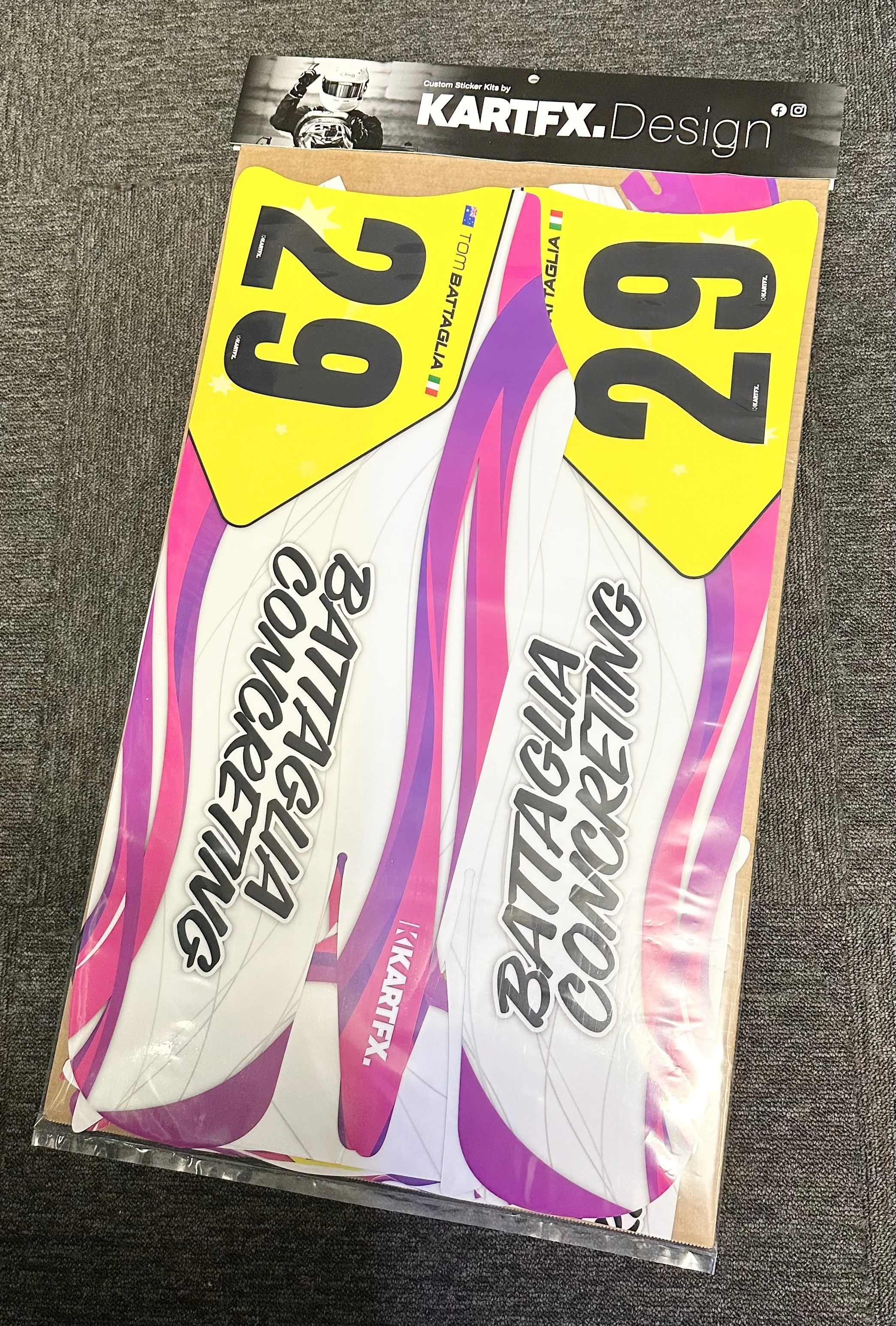Colorful decals for dirt bikes or motocross bikes showing 'BATTALION 20 E' and 'BATTALION 23 E' in black text, with pink, purple, and white backgrounds, inside a plastic sleeve on a gray textured surface.