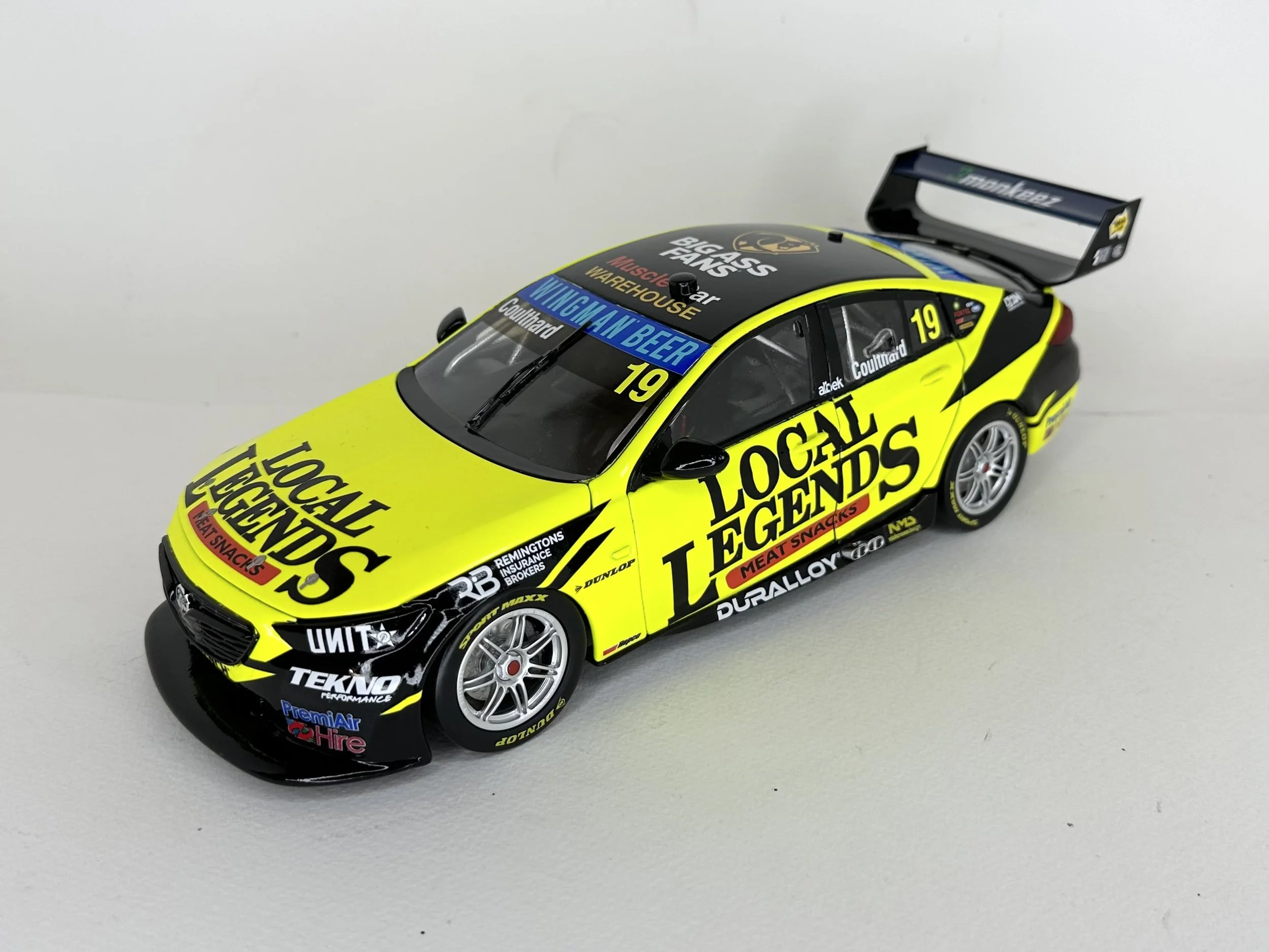 A yellow and black racing car with sponsor logos and the number 19 on the side and hood, positioned on a light-colored surface.