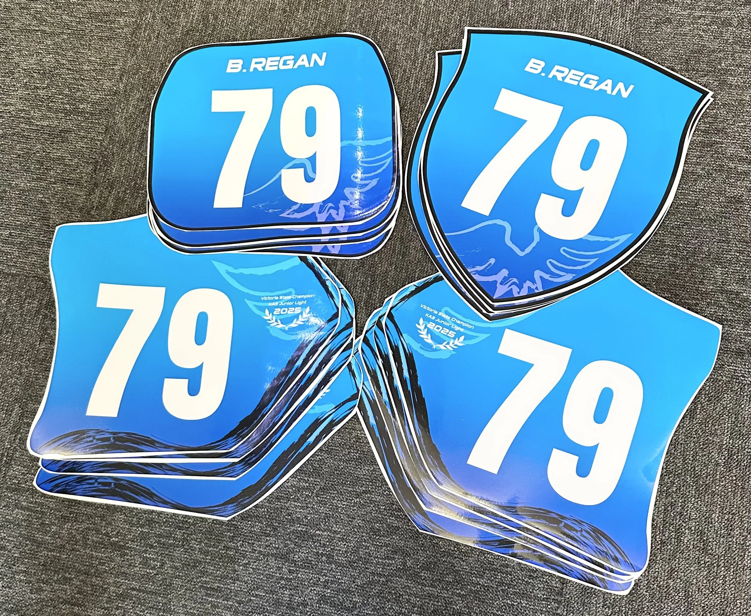 Stacks of blue stickers with the number 79 and the name B. REGAN, along with the text "Victoria State Champion 2025, KAB Junior Light."