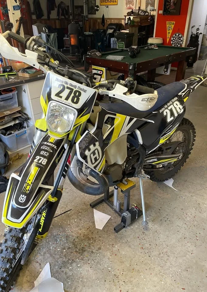 A dirt bike with racing number 278 in a garage or workshop, surrounded by tools and equipment.