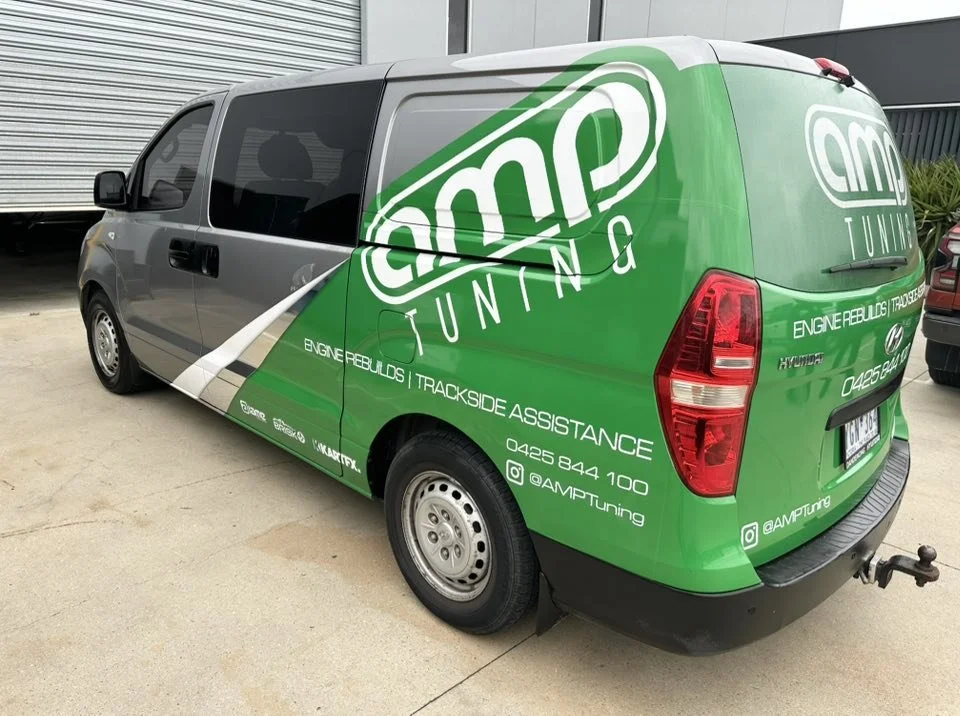 Green and gray van with AMP Tuning branding, contact info, and social media handles for automotive tuning services.