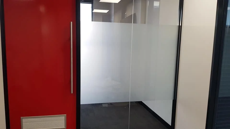 Glass office door with frosted inscription on inside, red wall on the left, and office interior visible through the glass.