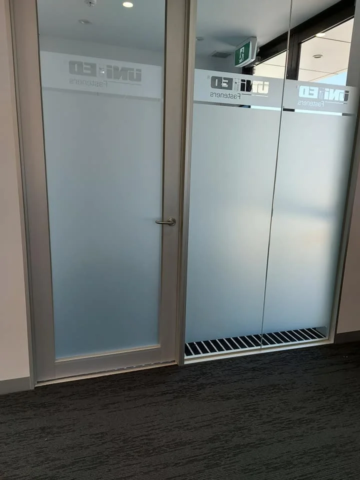 Frosted glass door with a small window and a handle, separating from another glass door, with an exit sign above.