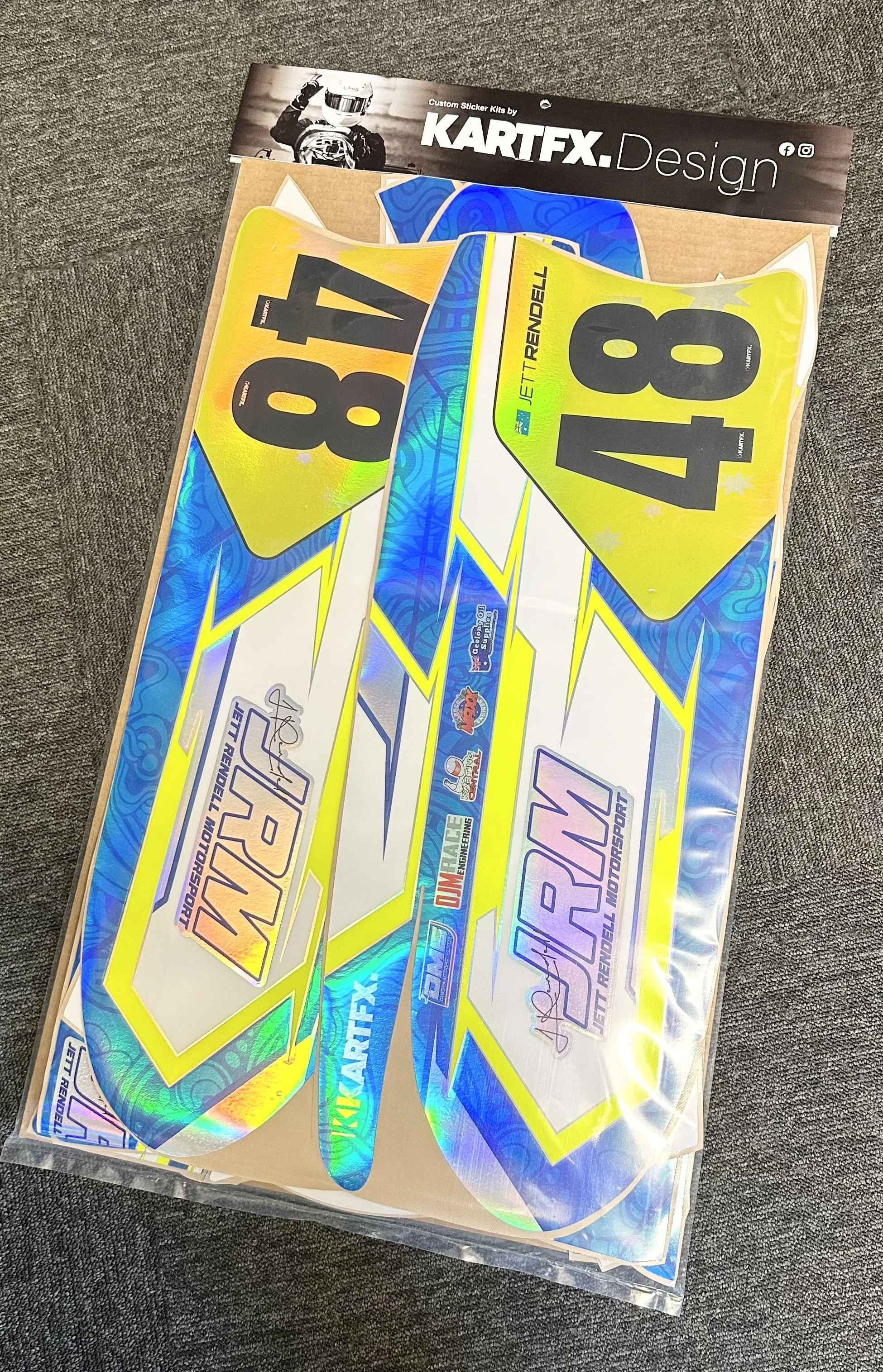 Holographic racing decals including number 48 decals and a Kartfx Design branding sticker, all laid out on a brown cardboard backing.