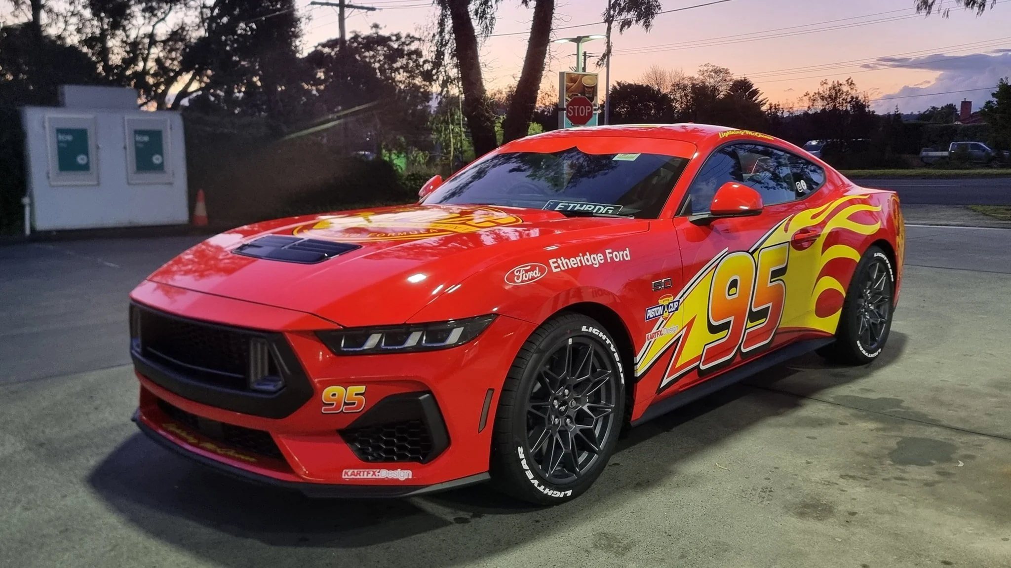 Red Chevrolet Corvette race car with flames and number 95 decals, parked in a lot at dusk.