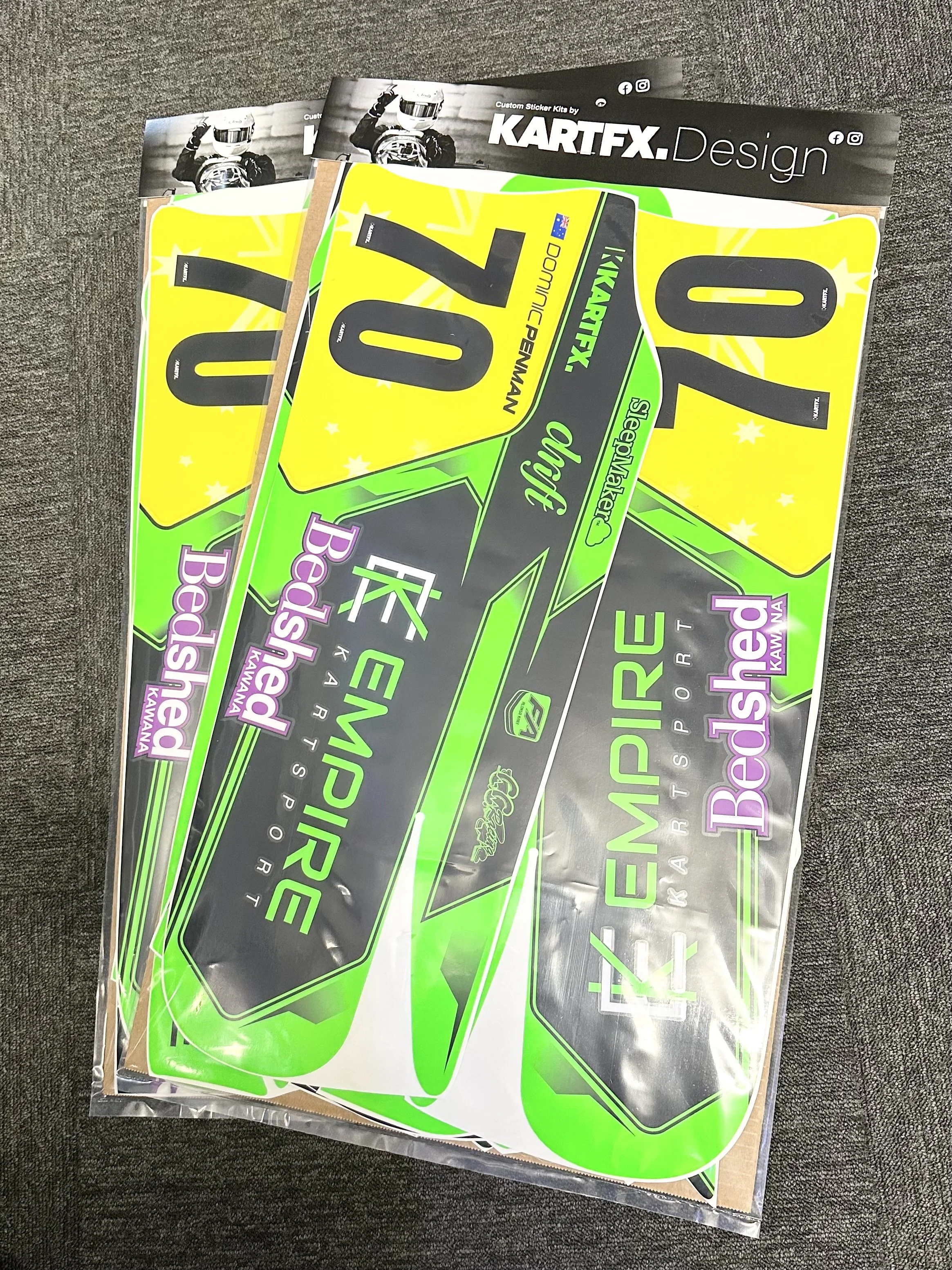A collection of colorful vehicle decals, including green, yellow, black, and purple stickers, for a racing car, displayed on a gray surface.