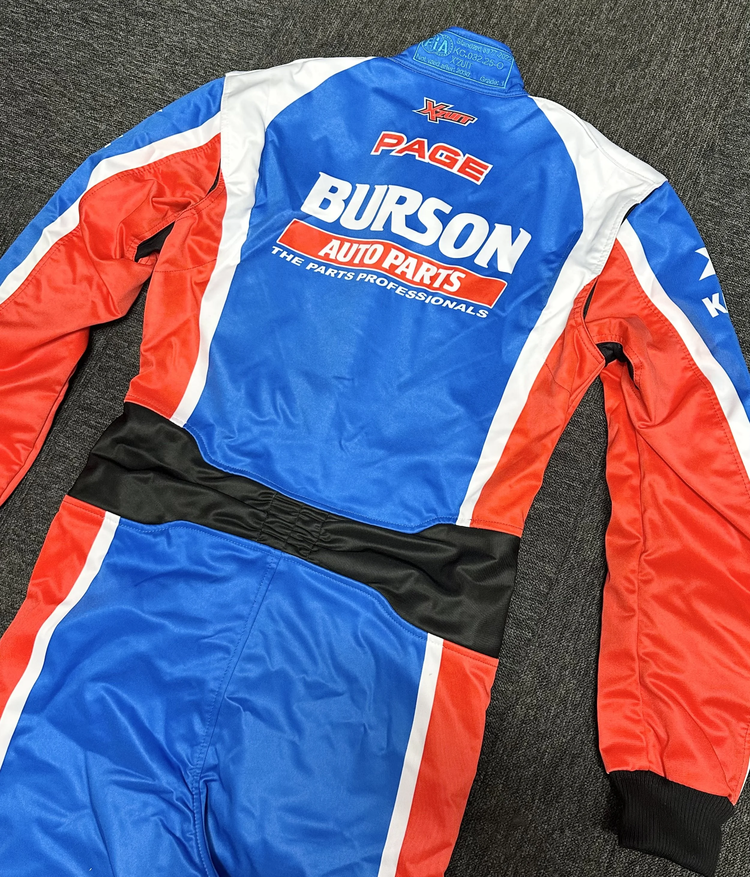 A racing suit with blue, red, white, and black colors, displaying logos of sponsors including Page, Burson Auto Parts, and Xtreme.