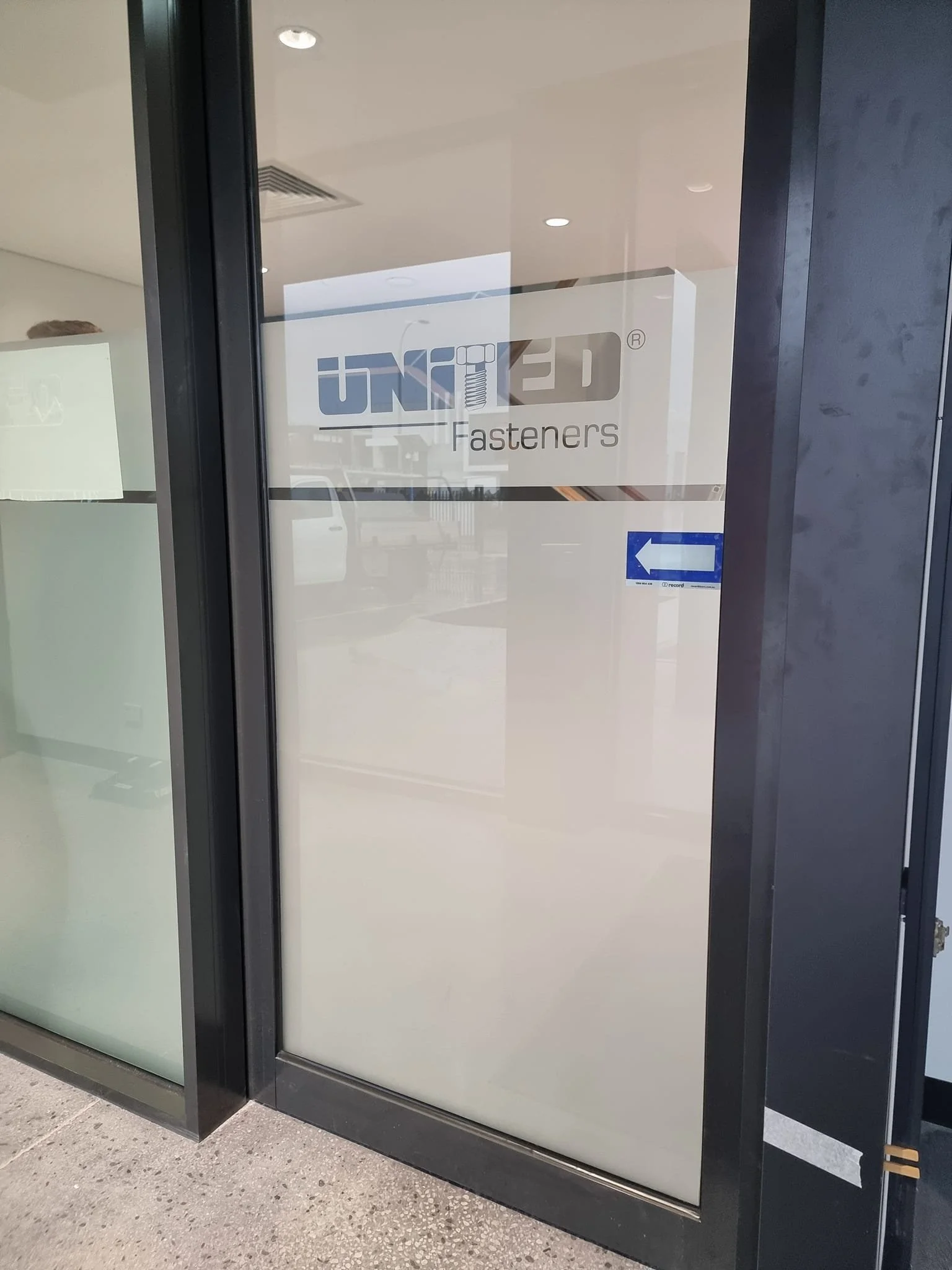 Glass door with a sign for United Fasteners, featuring a blue arrow pointing left.