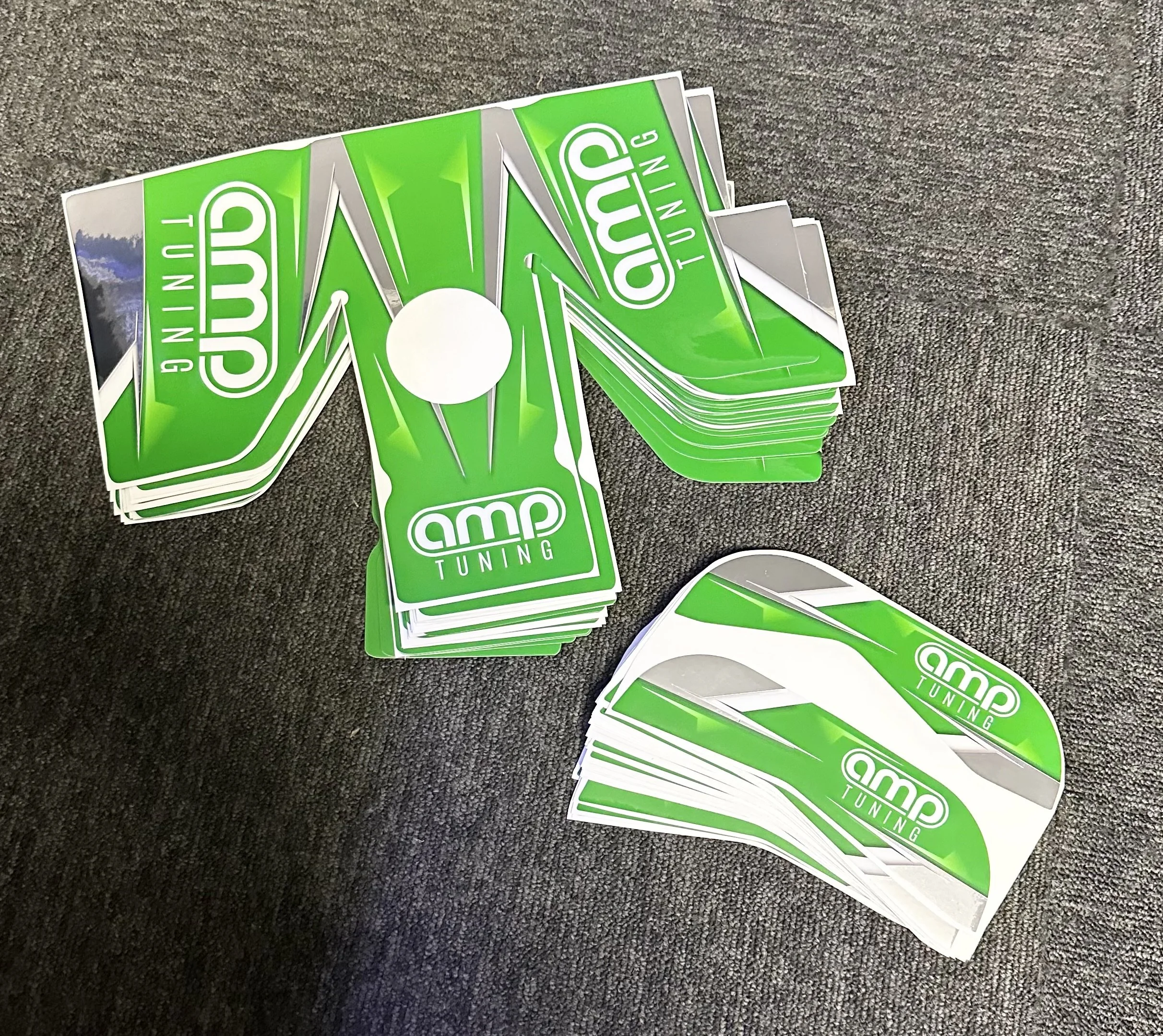 A collection of green and white stickers with the logo and text 'amp TUNING' on a dark gray fabric surface.
