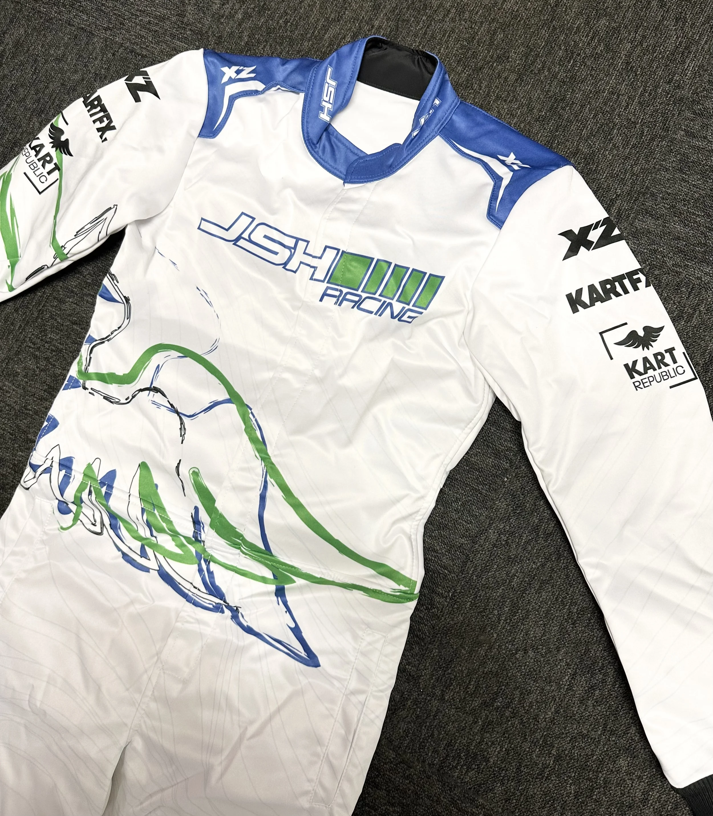 Racing suit with logos and graphics in white, blue, and green colors, lying on a dark surface.