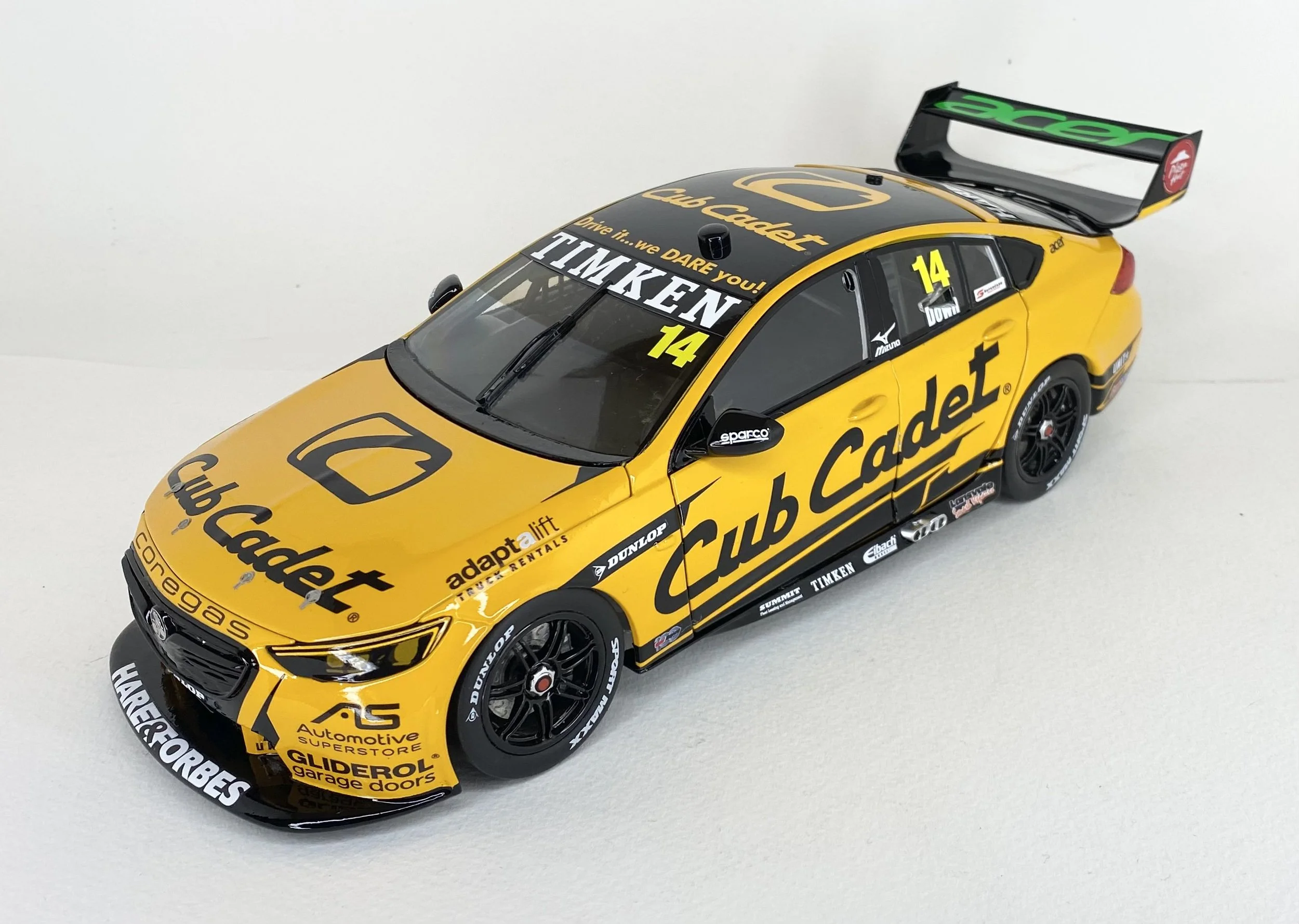 A detailed model of a yellow race car with black accents and sponsor decals, featuring a large rear wing and a black front splitter, on a white background.