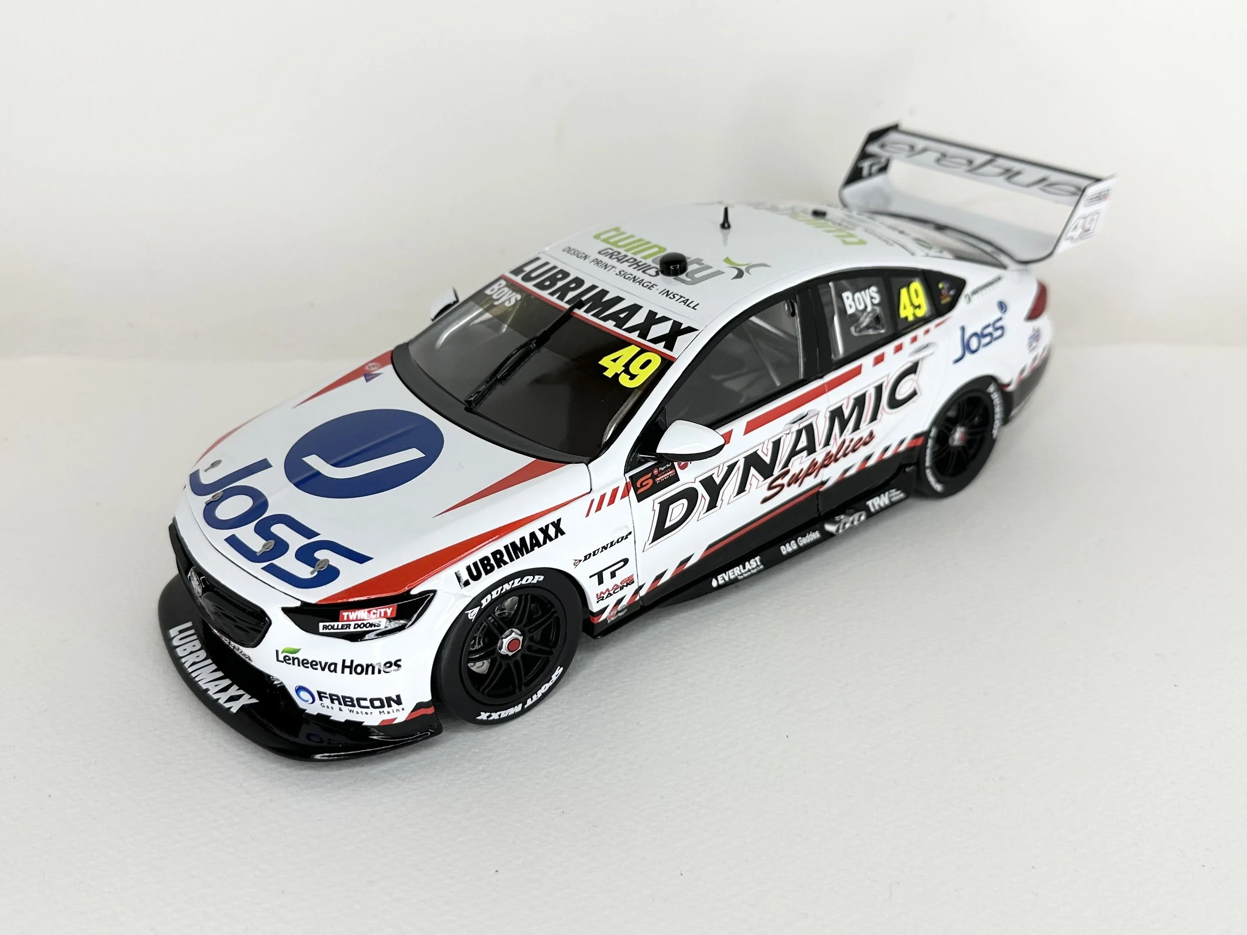 Scale model of a racing car with sponsor decals, black wheels, and a large rear wing, positioned on a white background.
