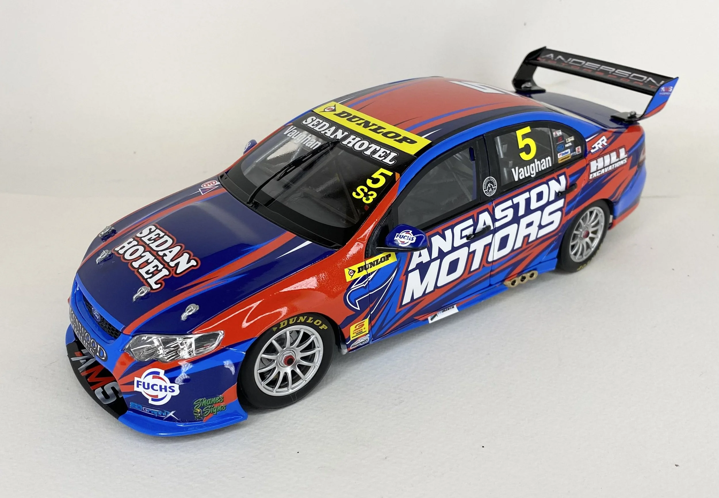 Model race car with blue, red, and black livery, sponsor logos, racing decals, and a rear wing.