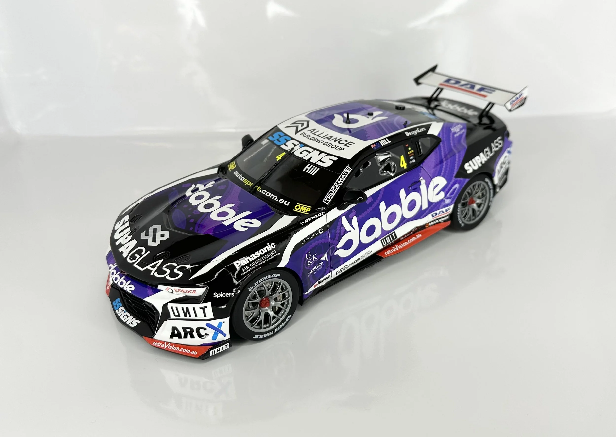 Scale model of a racing car with purple, black, and white sponsorship decals, featuring a large rear wing and detailed wheels.