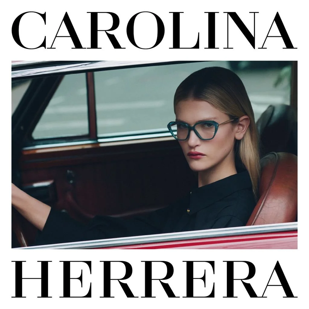 A woman with blonde hair and blue glasses sitting in a vintage car, looking at the camera, with a serious expression, with the text 'Carolina Herrera' above and below her.